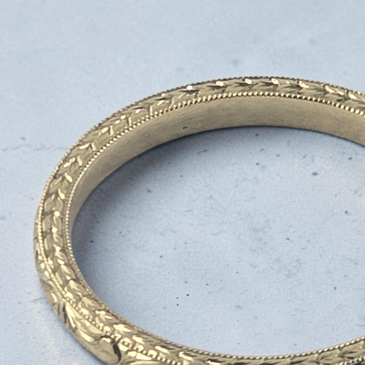 Close-up of two matching silver wedding or engagement rings with intricate hand engraved designs resting on a wooden surface.