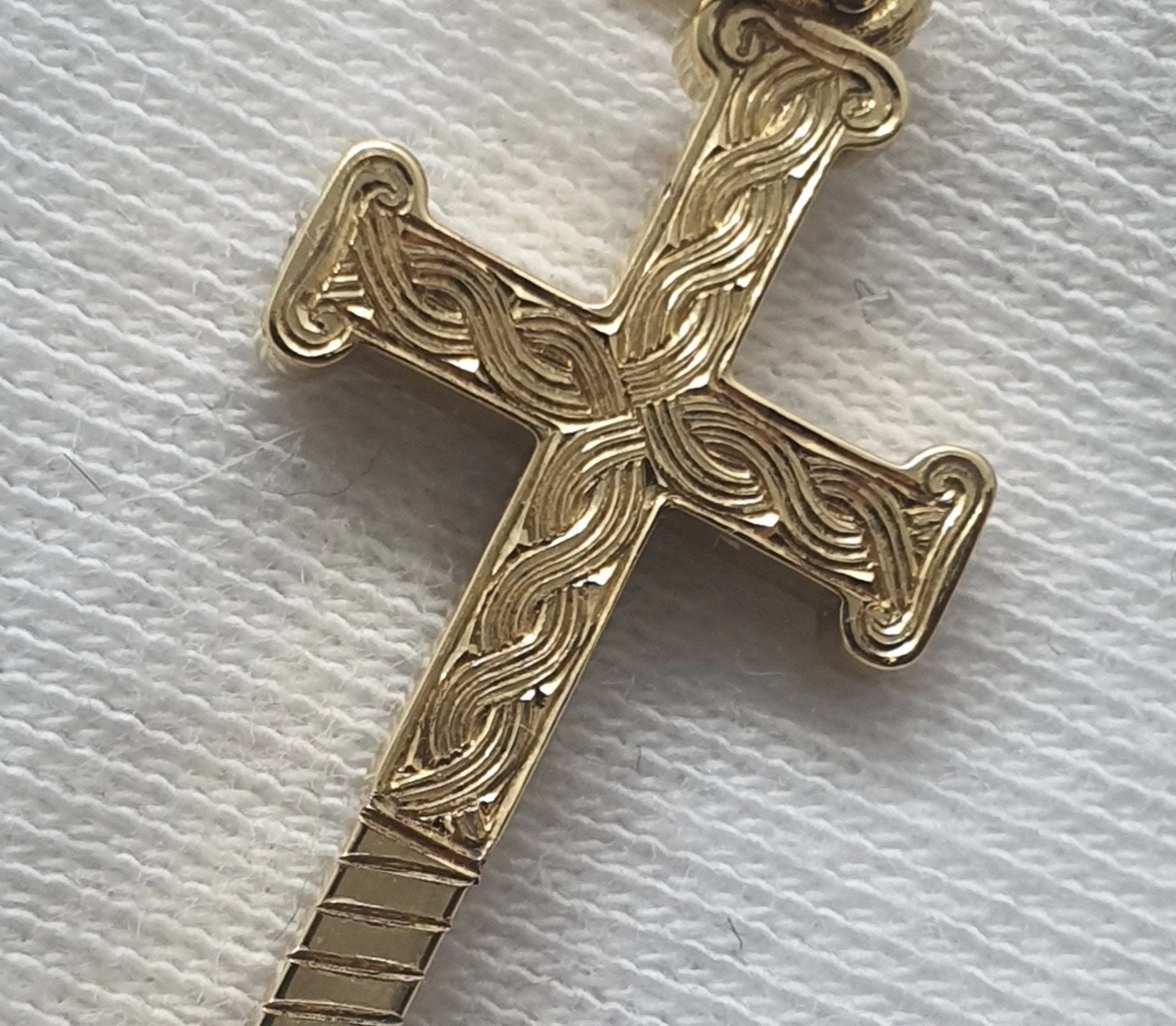 Close-up of a gold decorative cross with intricate hand engraved celtic swirling patterns.