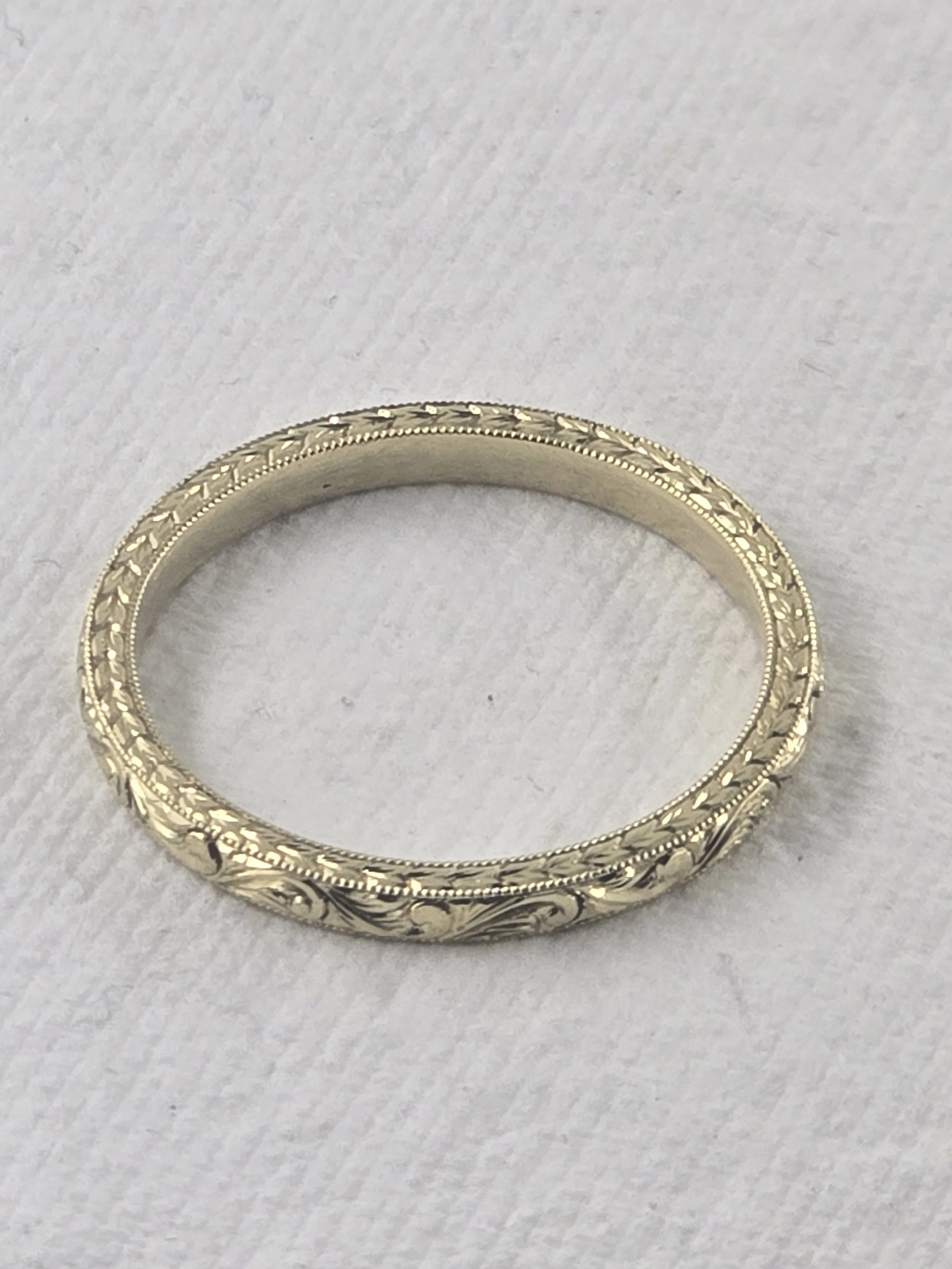 Gold ring with intricate vintage hand engraved floral and beaded design on a white textured background.