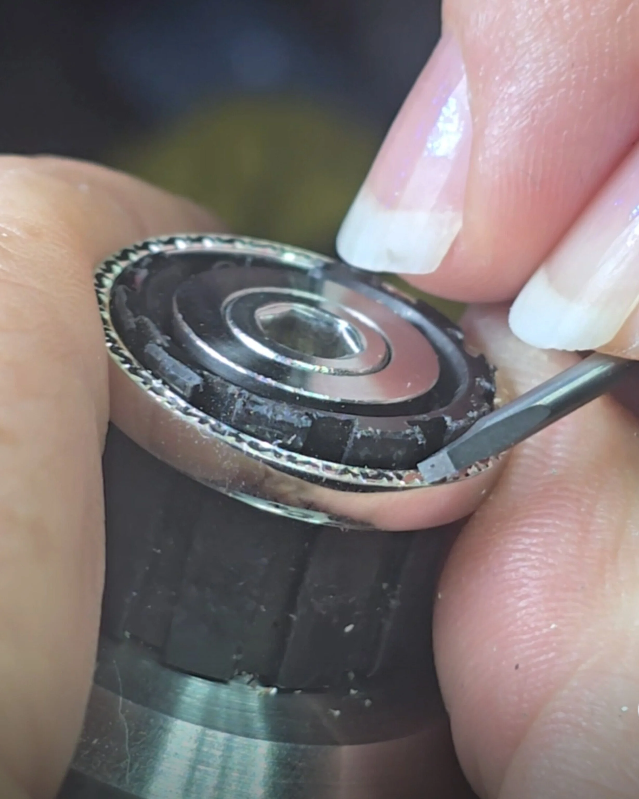 Close-up of a person's finger over a hand engraving tool, possibly in a workshop.