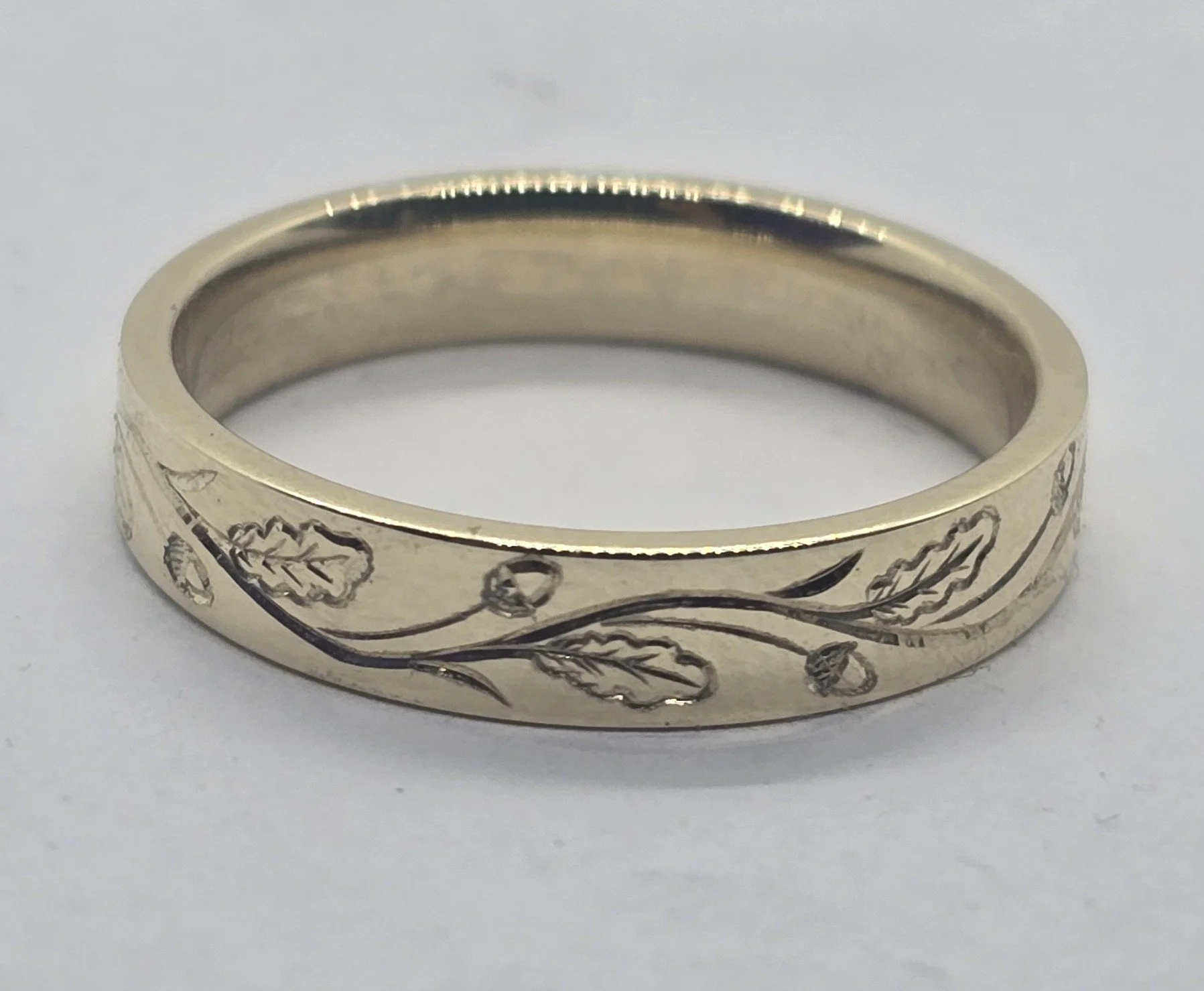 Close-up of a gold wedding or engagement band featuring a unique bespoke botanical hand engraved pattern.