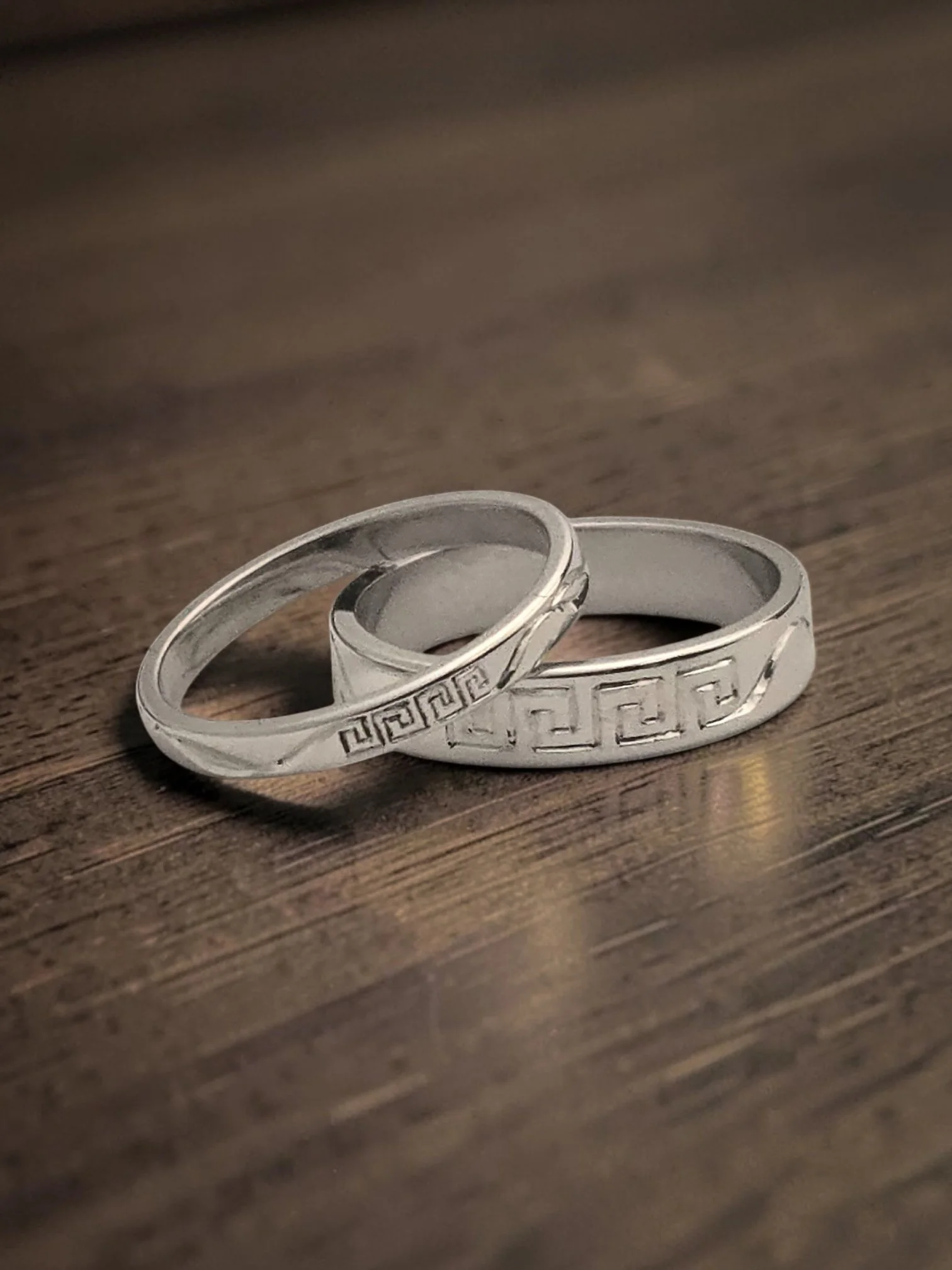 Close-up of two matching silver wedding or engagement rings with intricate hand engraved designs resting on a wooden surface.