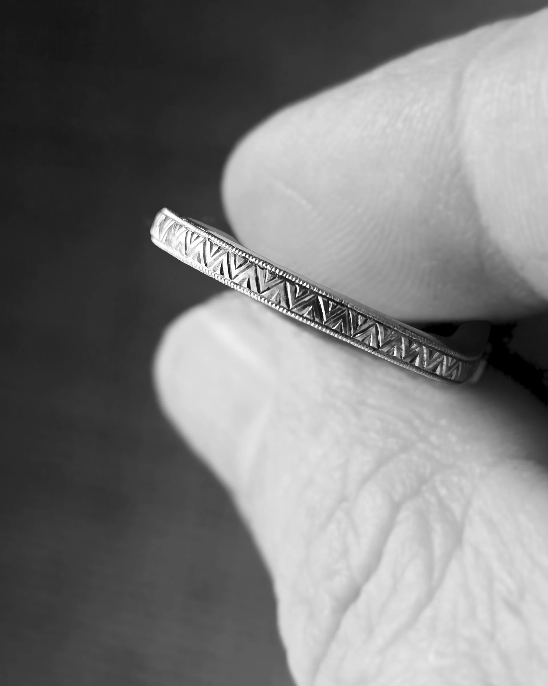 Close-up of a white gold engagement ring with intricate geometric patterns, held by a person's hand, featuring traditional fine hand engraving.