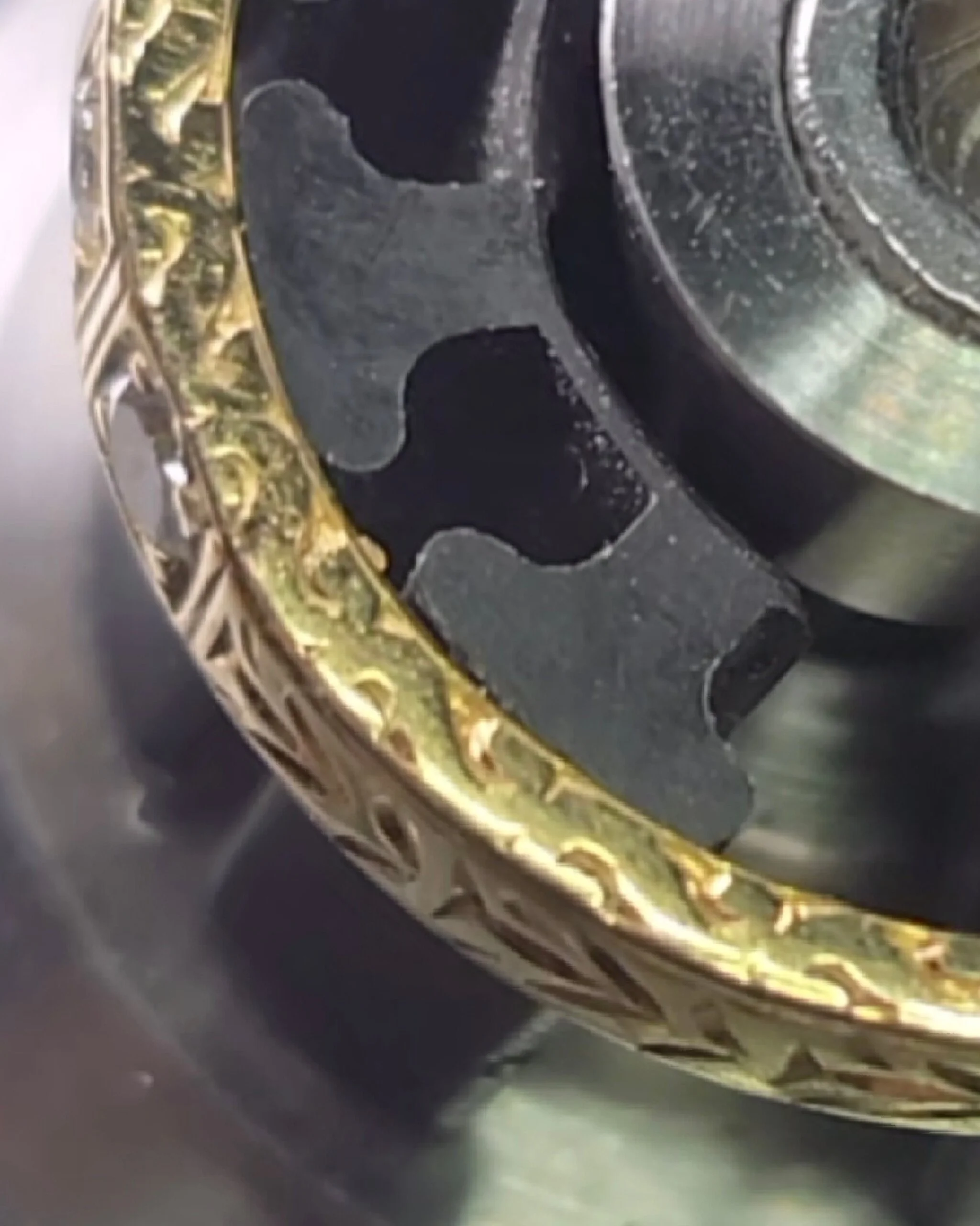Close-up of a gold and black decorative wedding band prior to being restored by hand engraving.