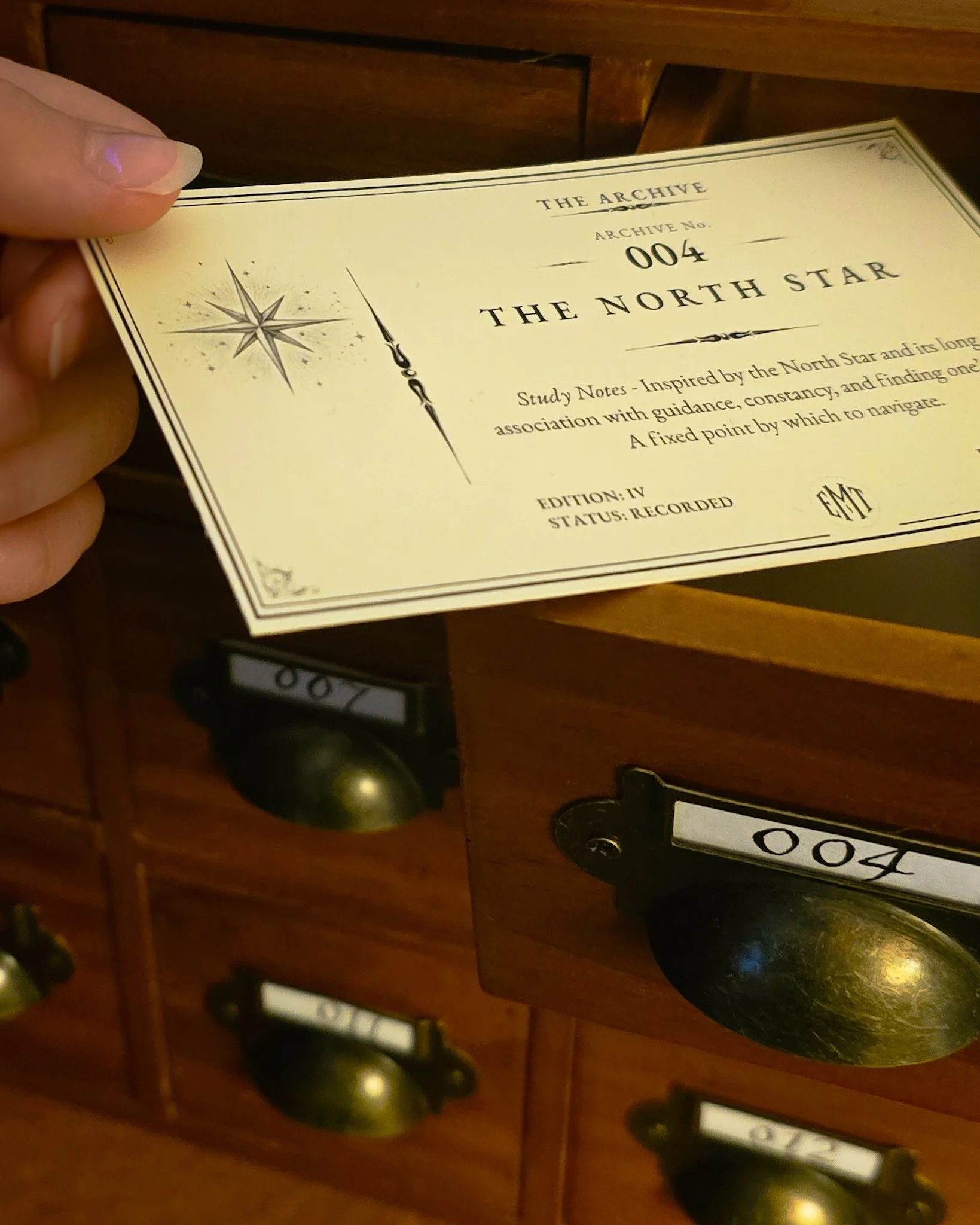 Close-up of vintage style mailbox tags on a wooden mail station, showing the number 004 on one and partially visible number 002 on another, with a warm indoor setting.