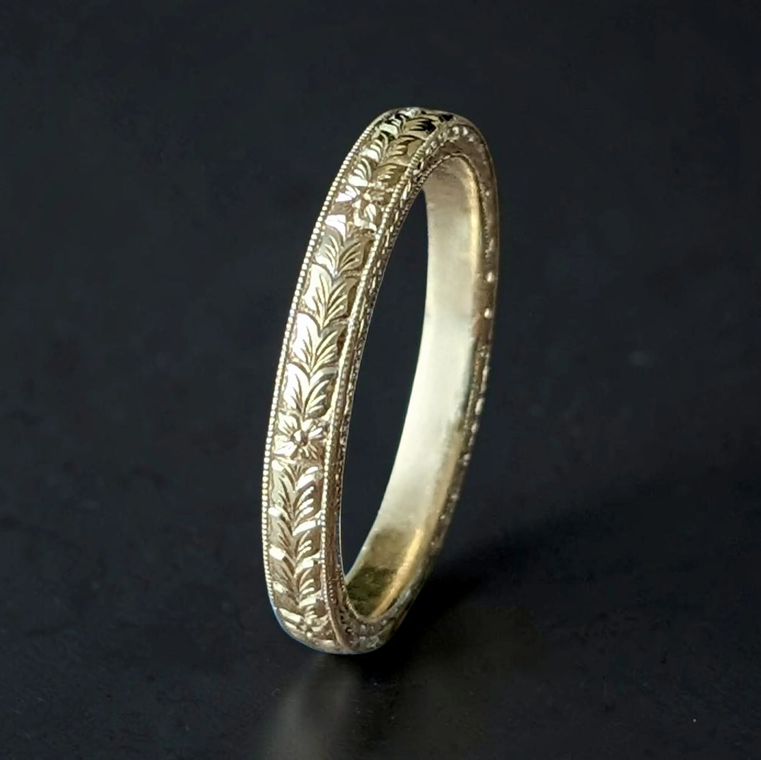 A detailed gold ring with intricate floral hand engravings on a black background.