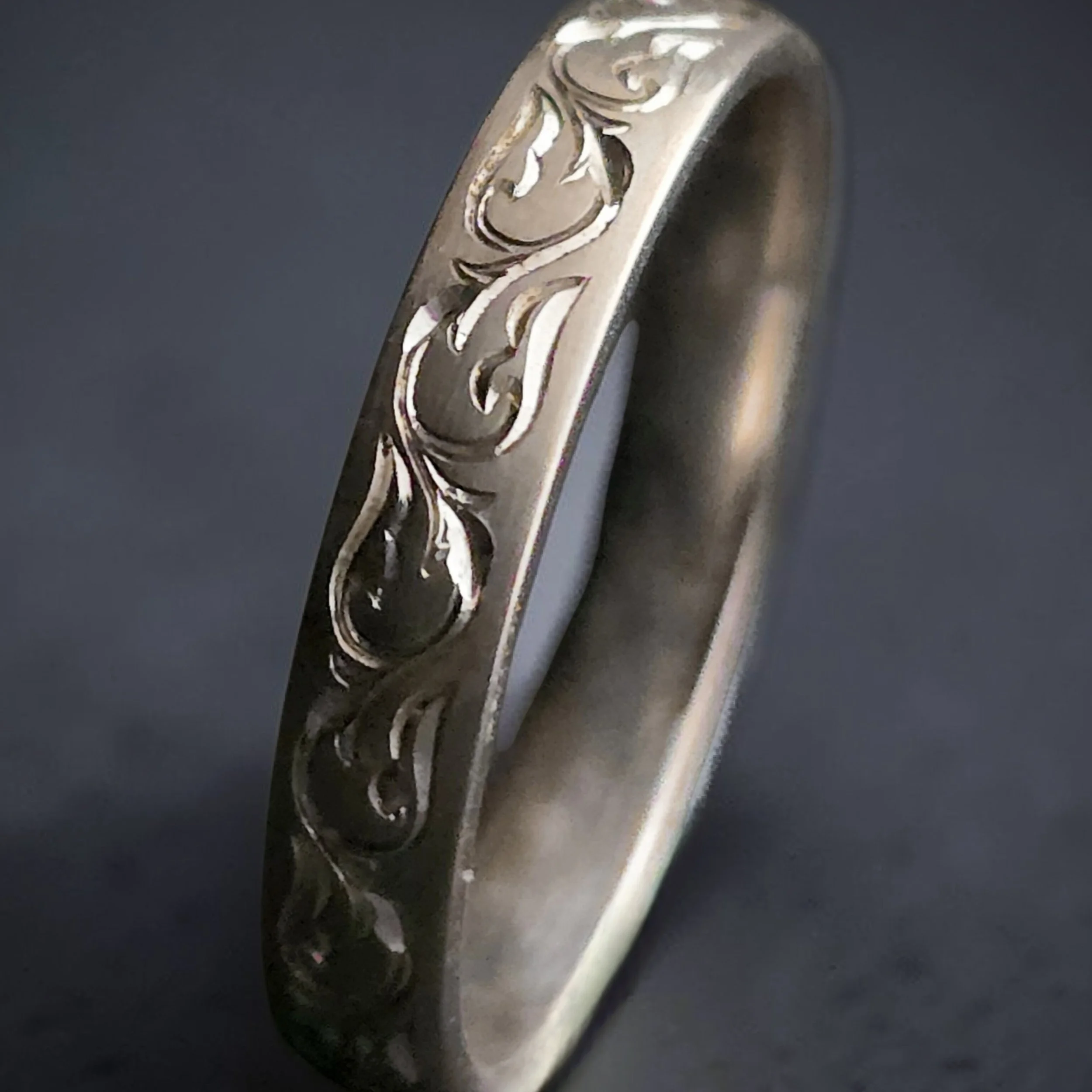 Close-up of a sterling silver wedding or engagement band featuring a unique bespoke botanical hand engraved pattern.