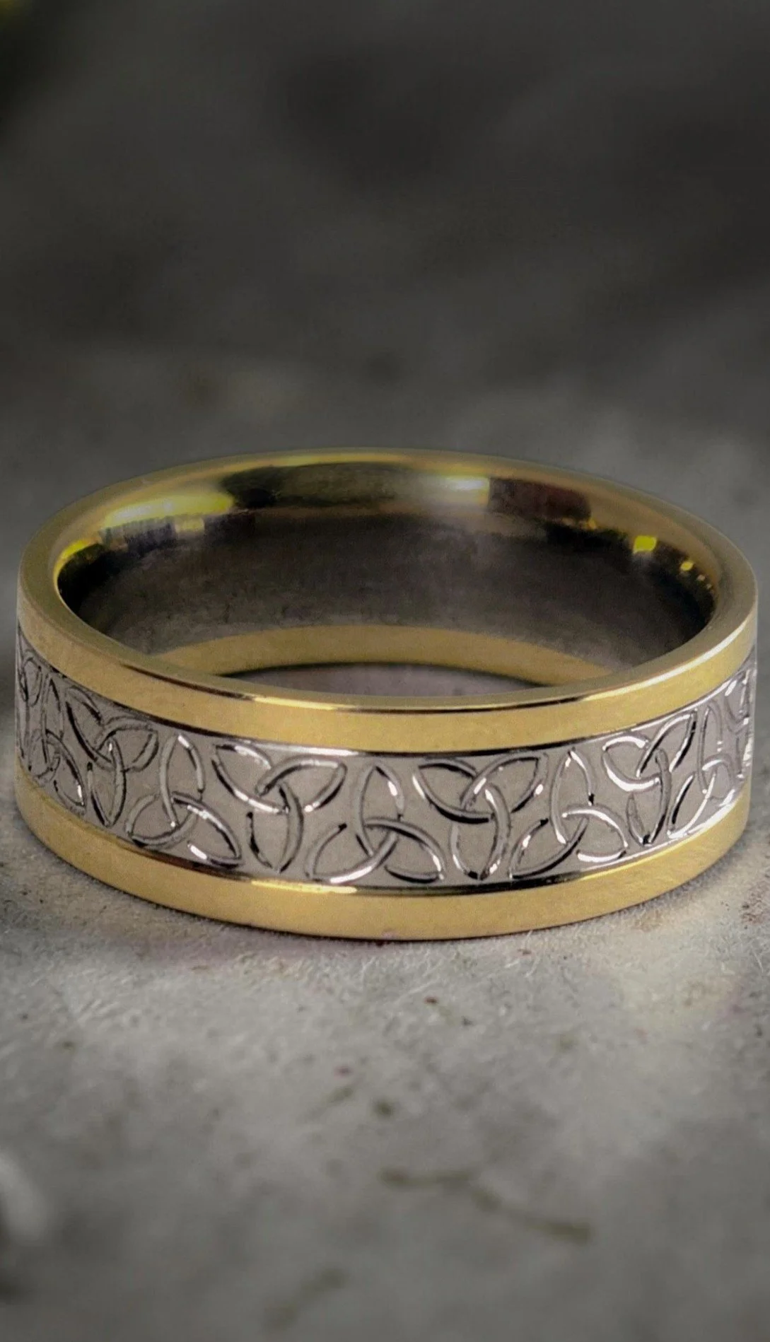 A hand engraved ring with gold and silver tones, featuring an intricate celtic knot design on the silver section.