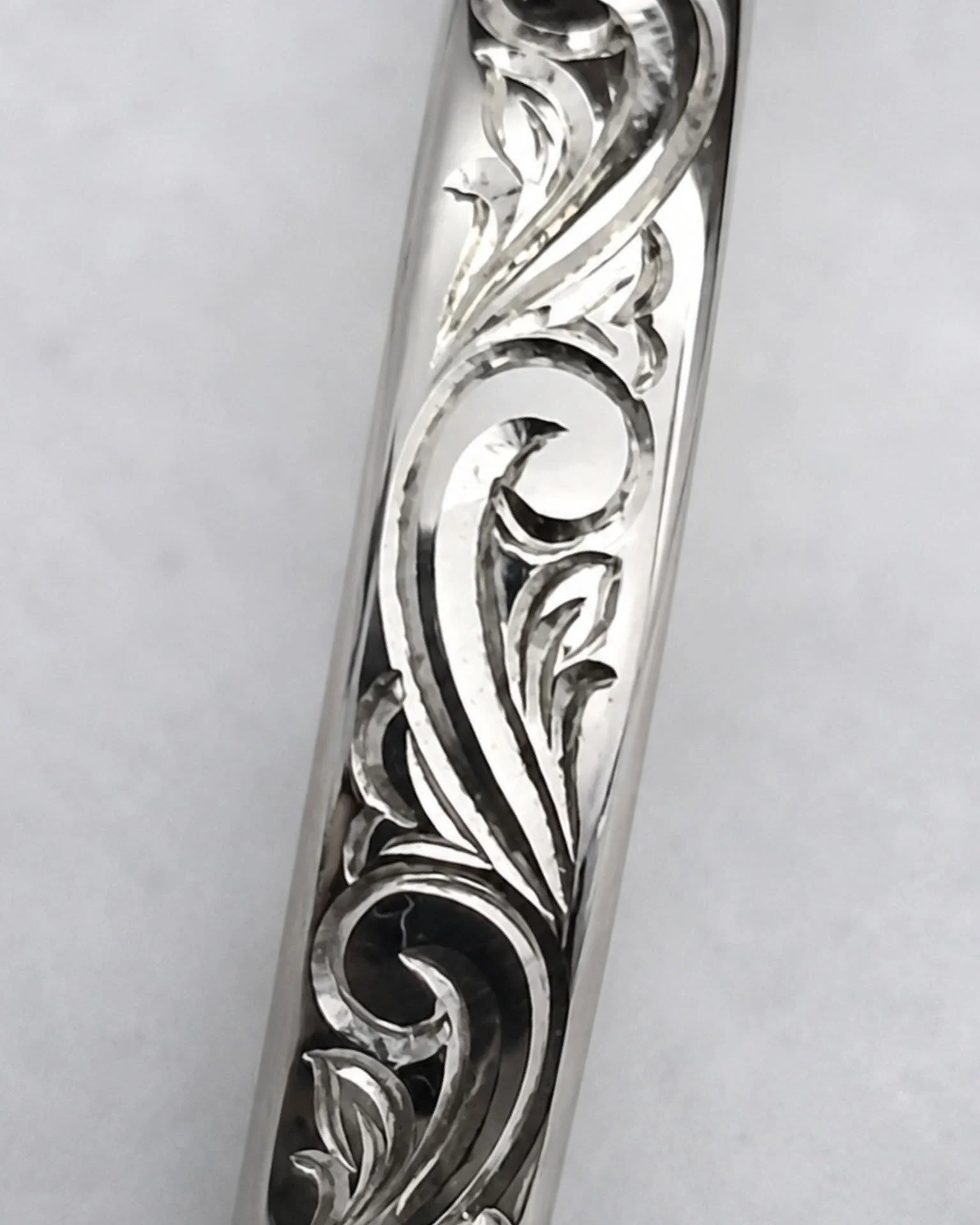Close-up of two matching silver wedding or engagement rings with intricate hand engraved designs resting on a wooden surface.