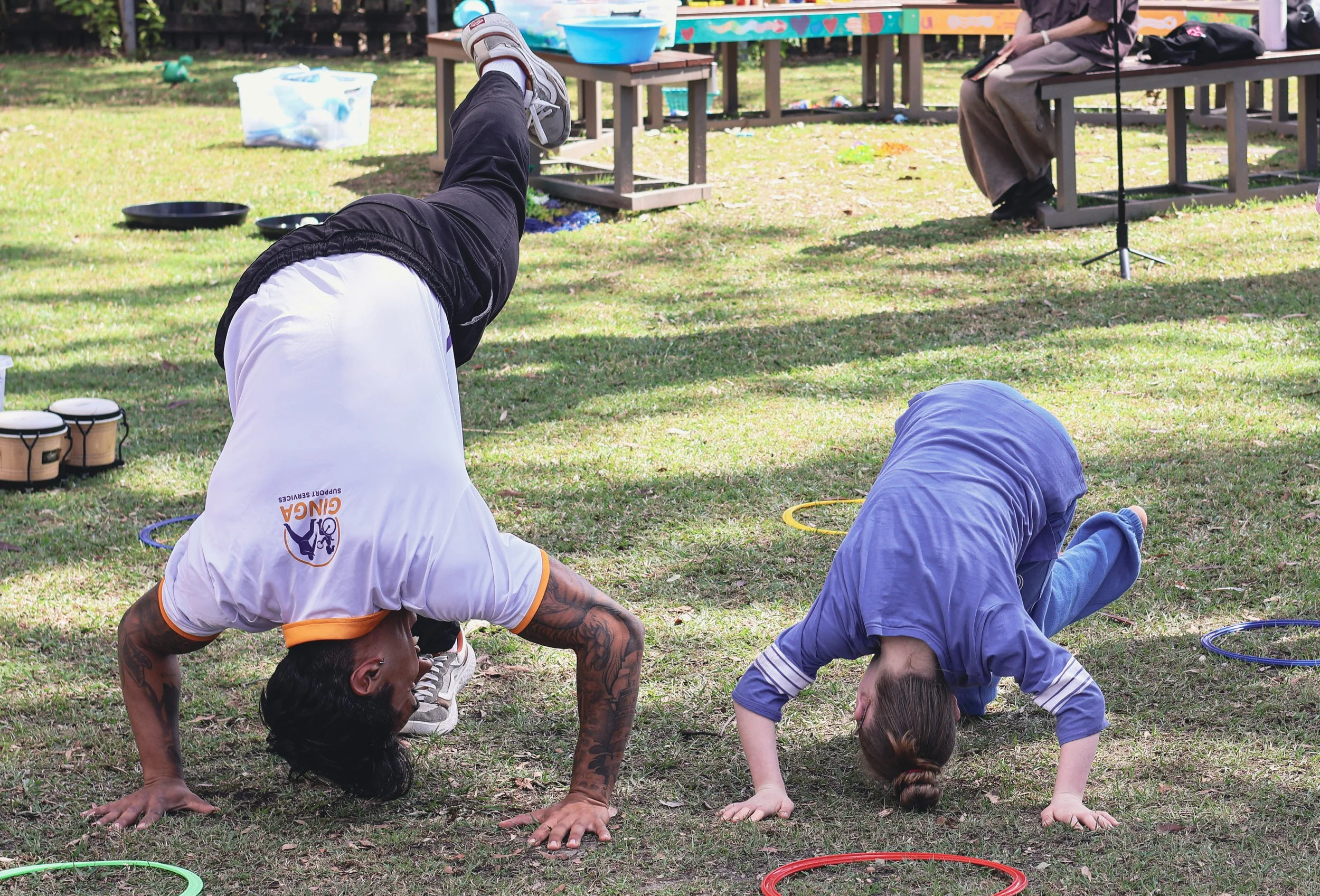 A young girl and adult instructor doing a handstand move as part of Capoeira martial arts on a lawn
