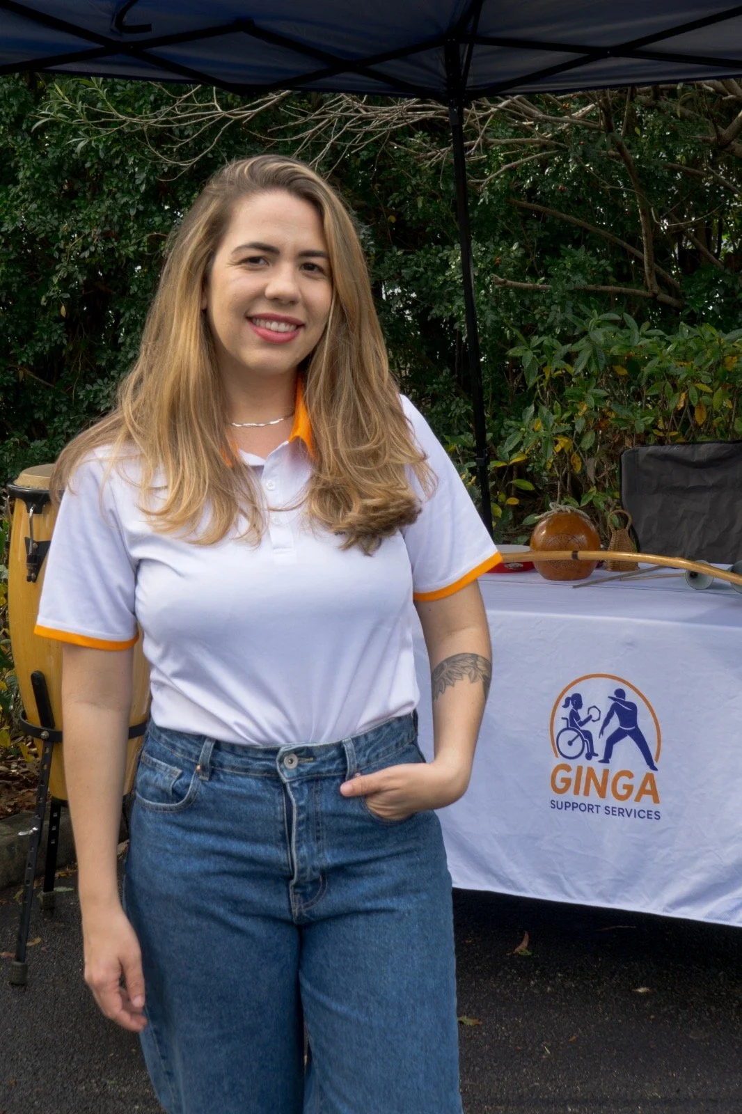 A woman with long blonde hair wearing a white polo shirt and jeans. She is smiling happily