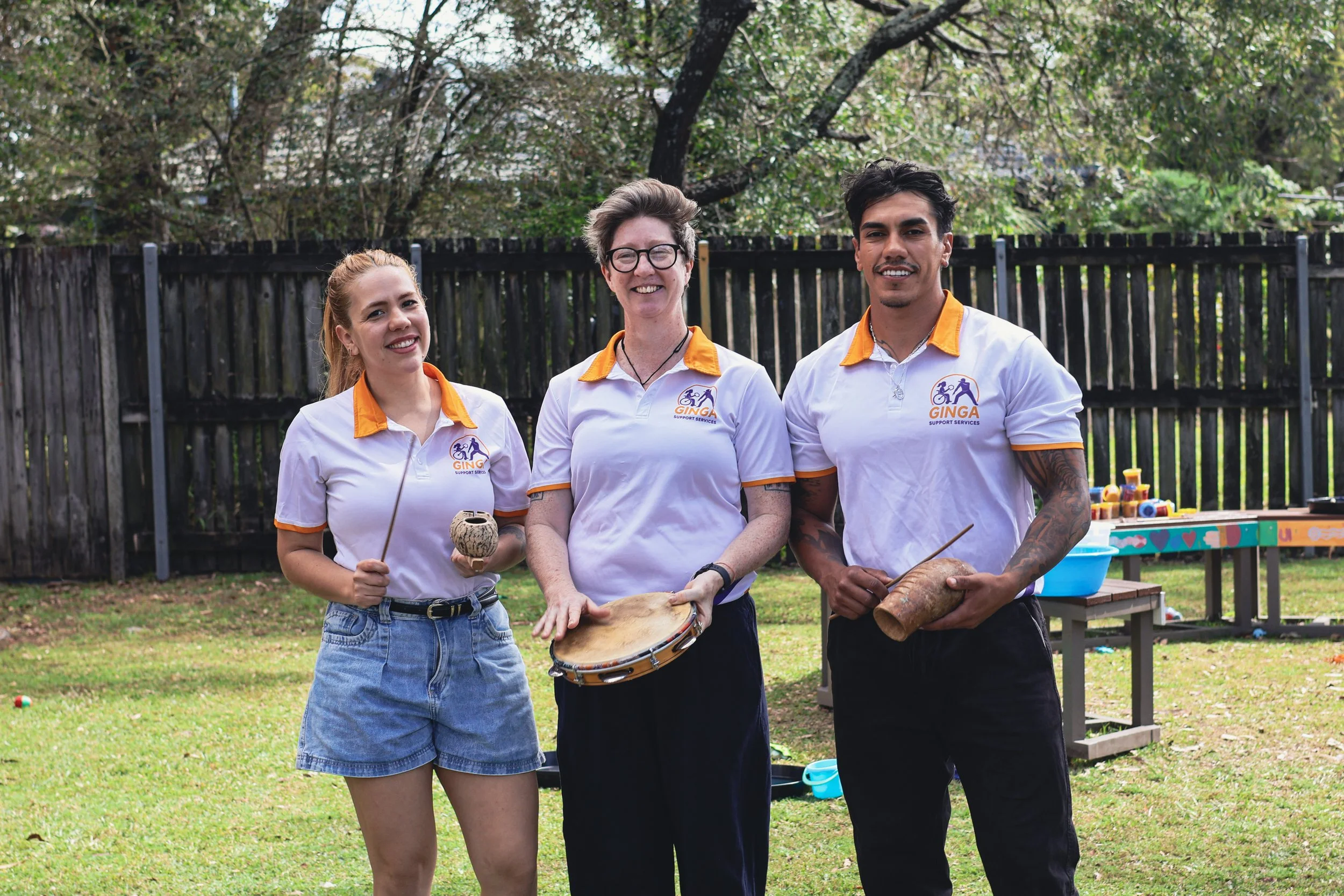Three people standing on a lawn holding Brazilian musical instruments.