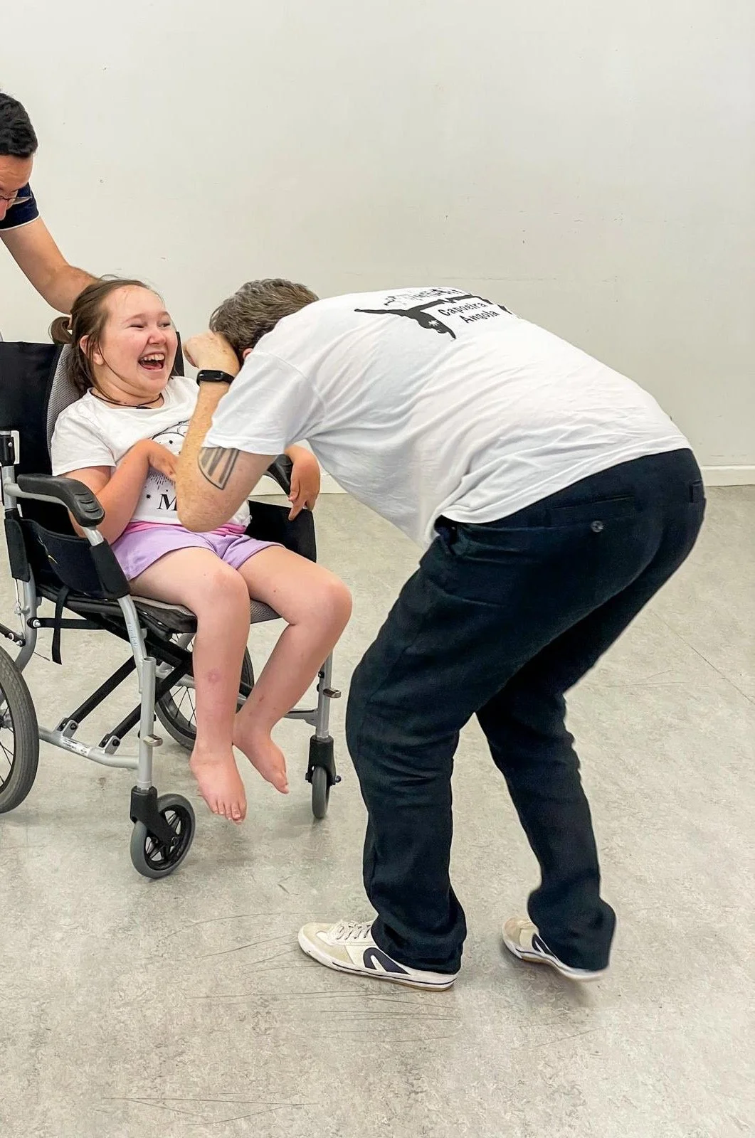 A disabled girl in a wheelchair and a Capoeira instructor dancing as part of a Capoeira martial arts class