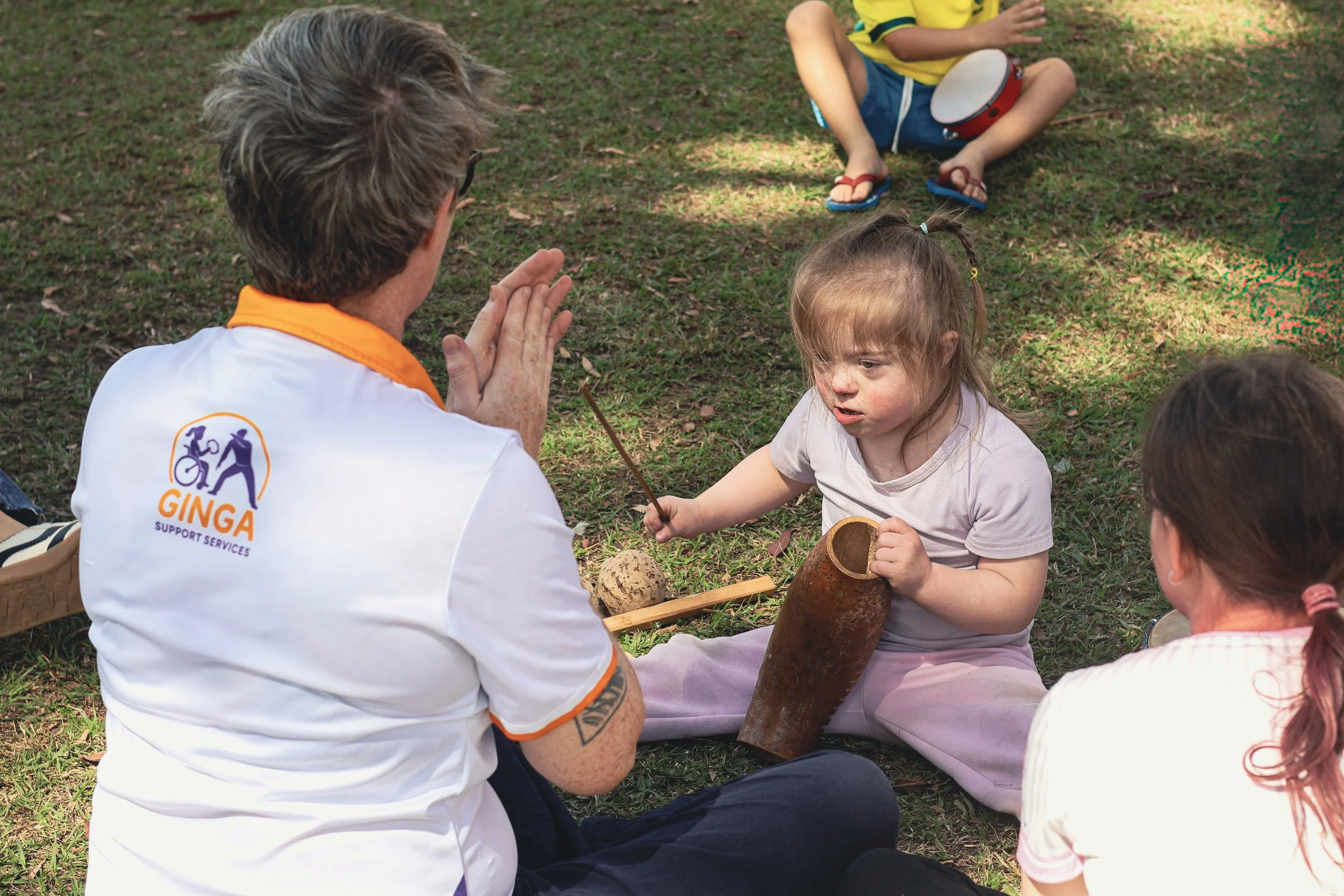 A young disabled girl playing a Brazilian instrument while sitting on grass as part of Capoeira martial arts