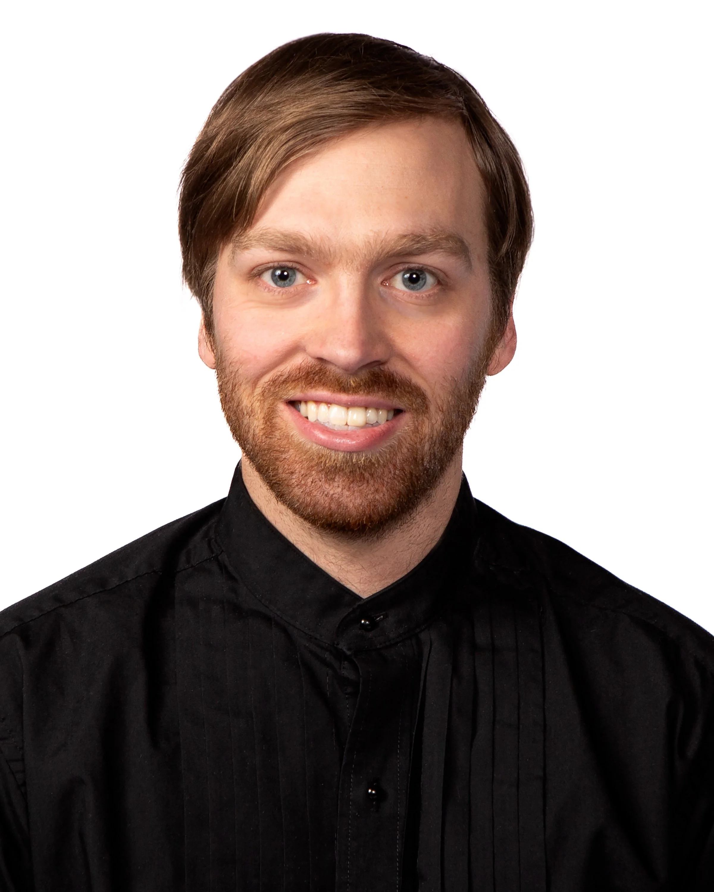 Close-up of a smiling man with blue eyes, brown hair, and a beard, wearing a black button-up shirt.