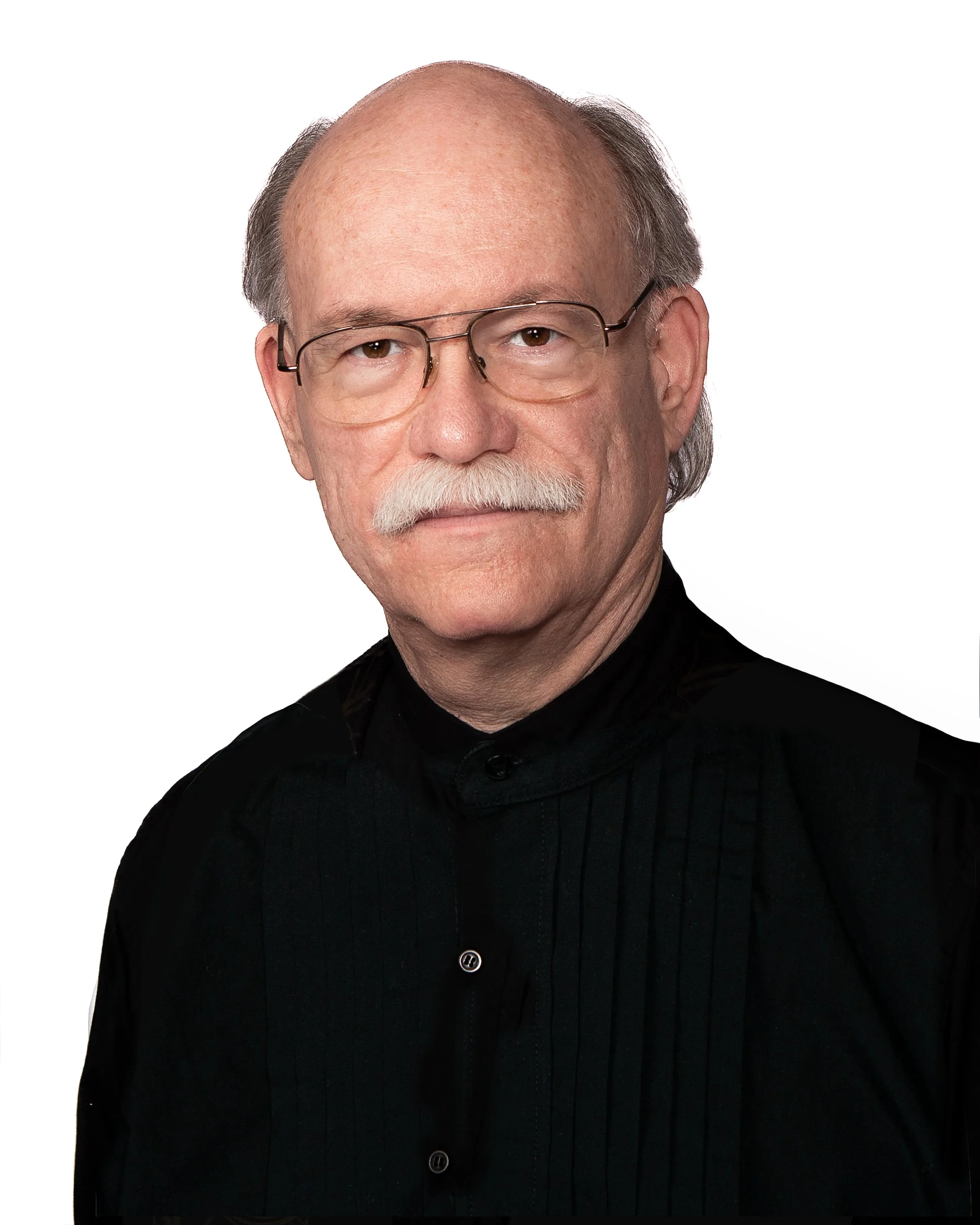Close-up portrait of a man with glasses, a white mustache, and a white goatee, wearing a black, pinstripe shirt against a white background.