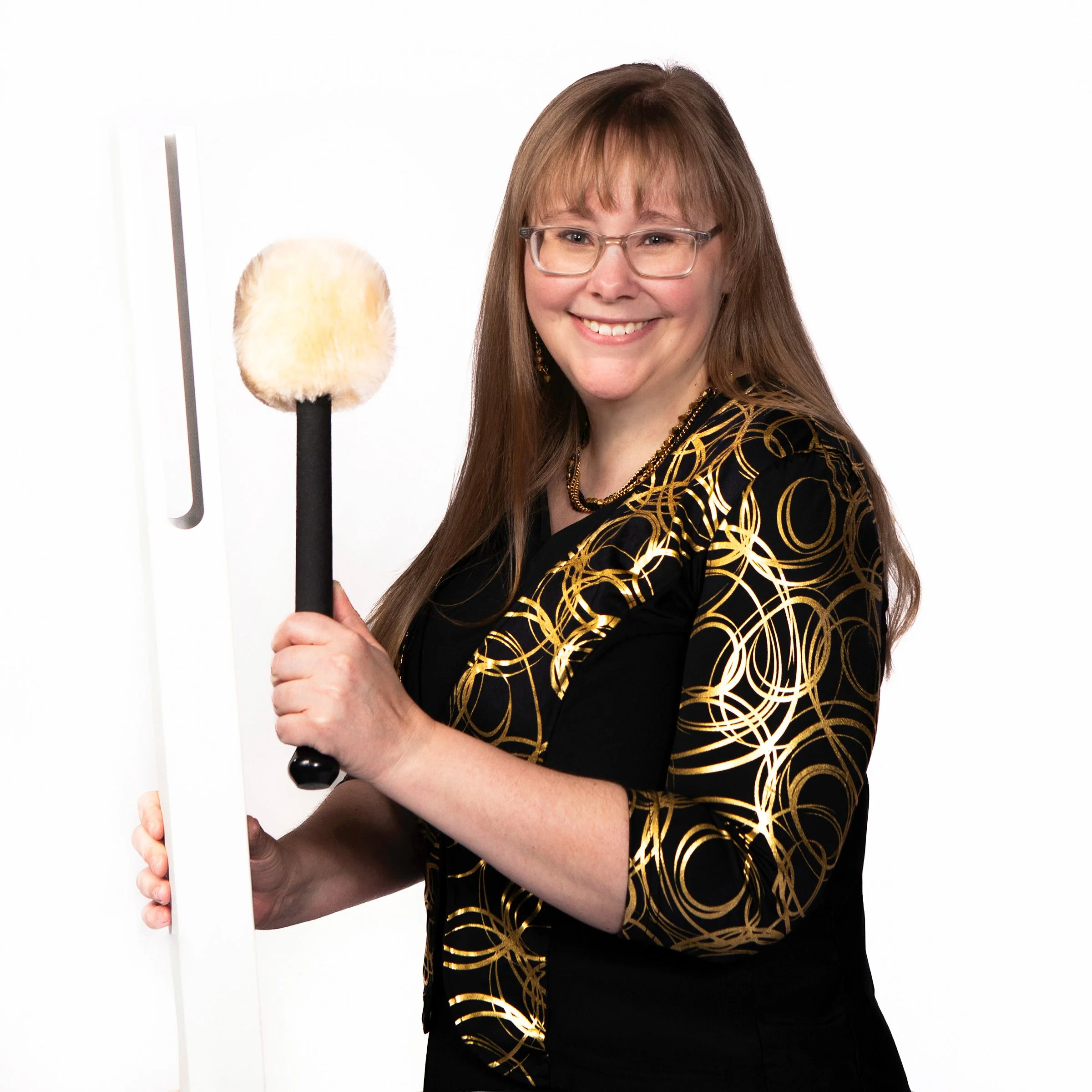 A smiling woman with brown hair, glasses, and a black and gold patterned dress, standing against a plain white background.