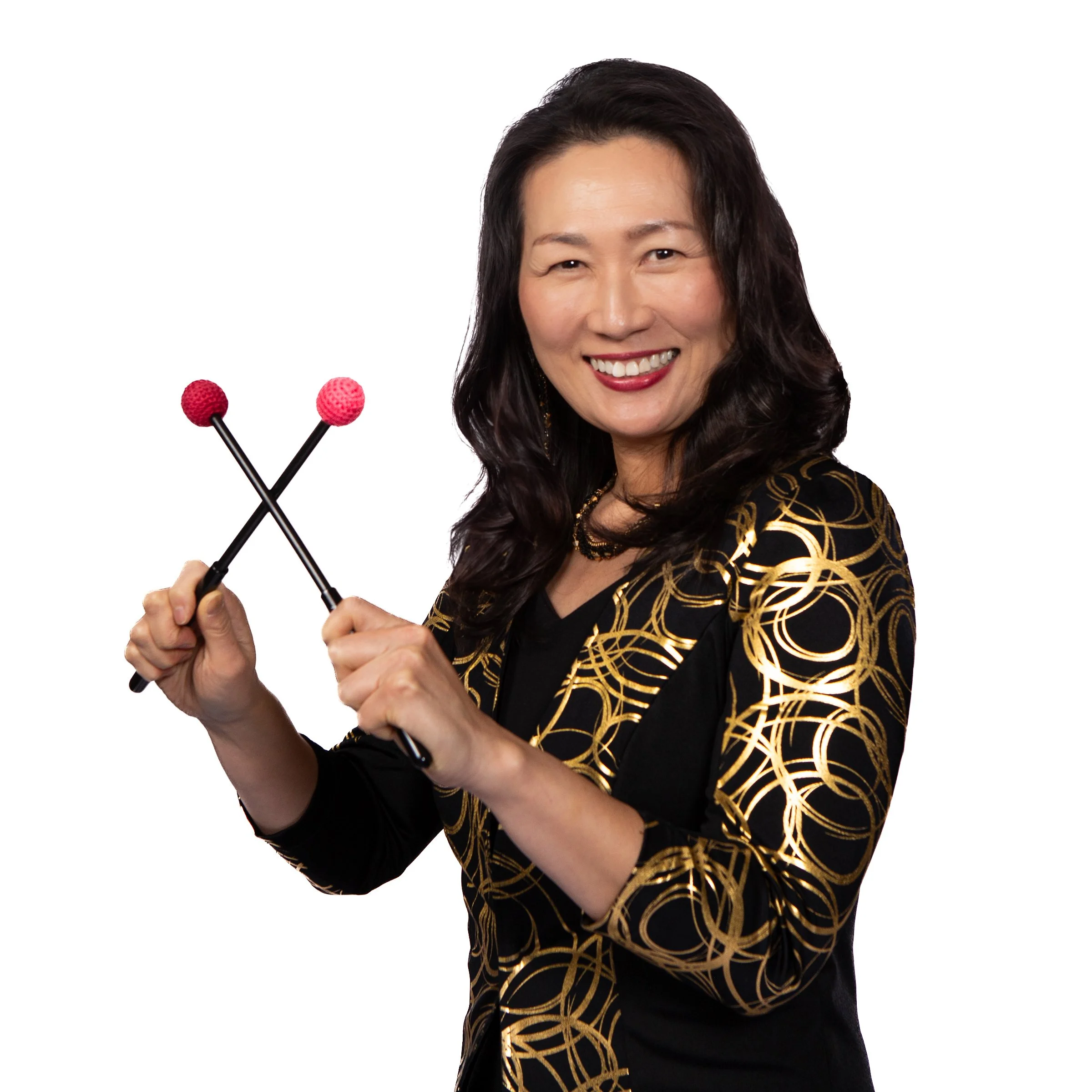 A woman smiling and holding a pair of black drumsticks with pink textured balls on the ends, against a plain white background.