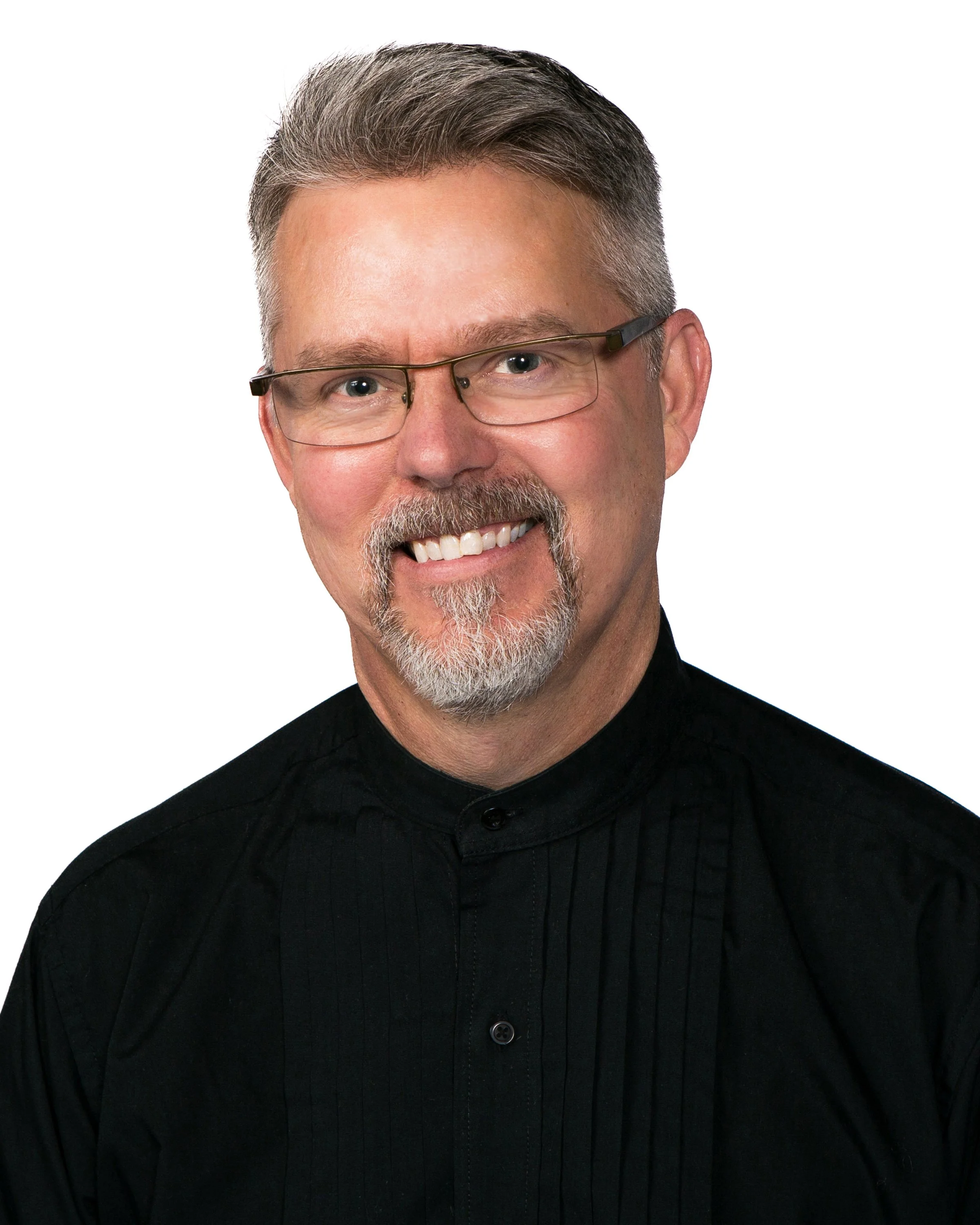 A  man with gray hair and beard wearing glasses and a black, high-collared sweater, smiling against a white background.