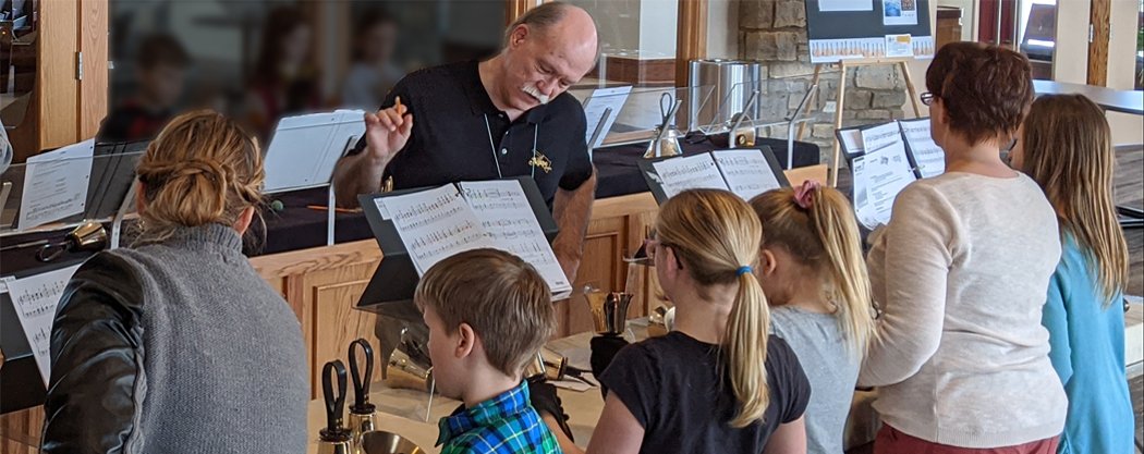 Music instructor teaching children music at a workshop, with sheet music and musical instruments visible.