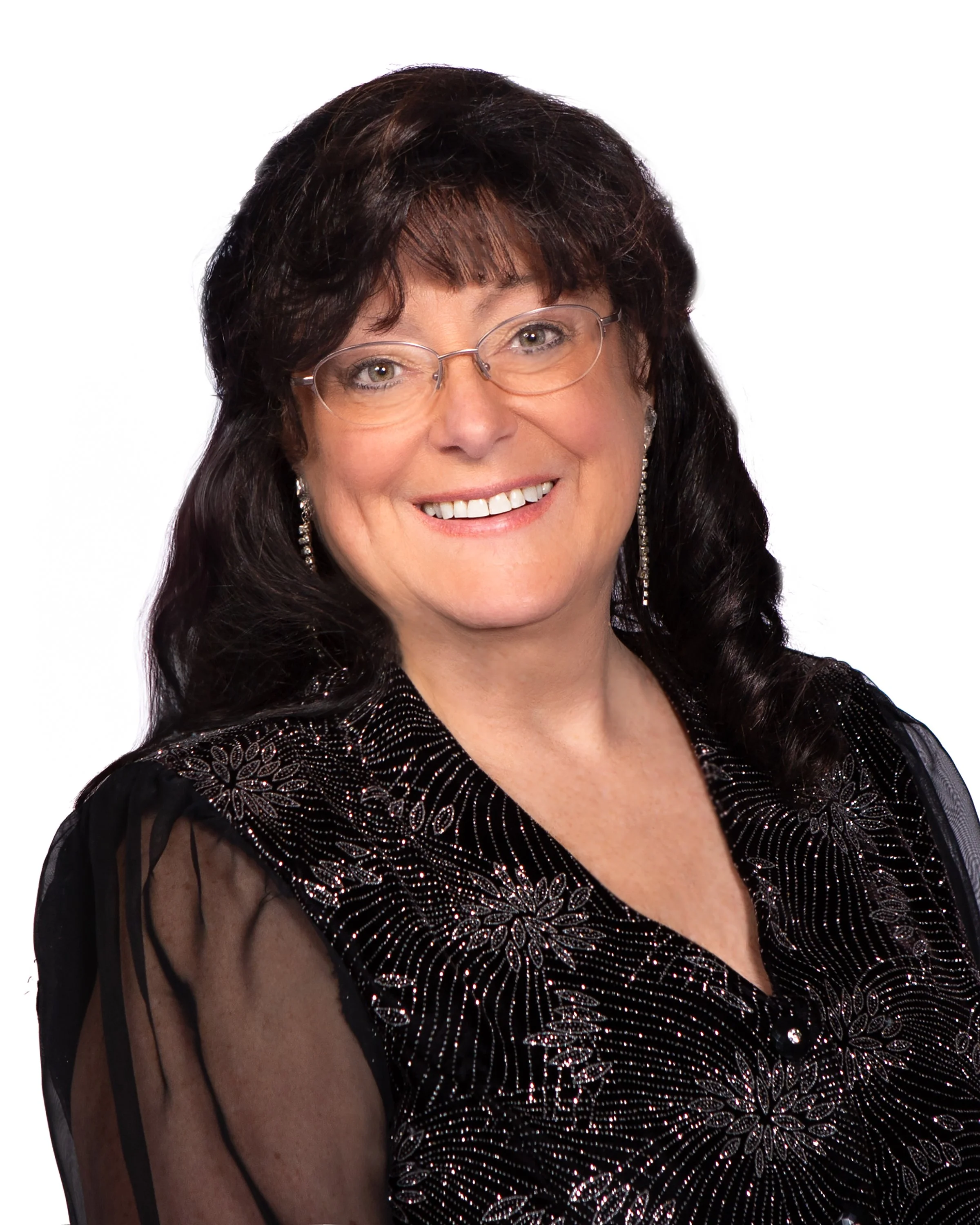 Close-up of a smiling woman with dark hair, glasses, earrings, and a black dress with embellishments.