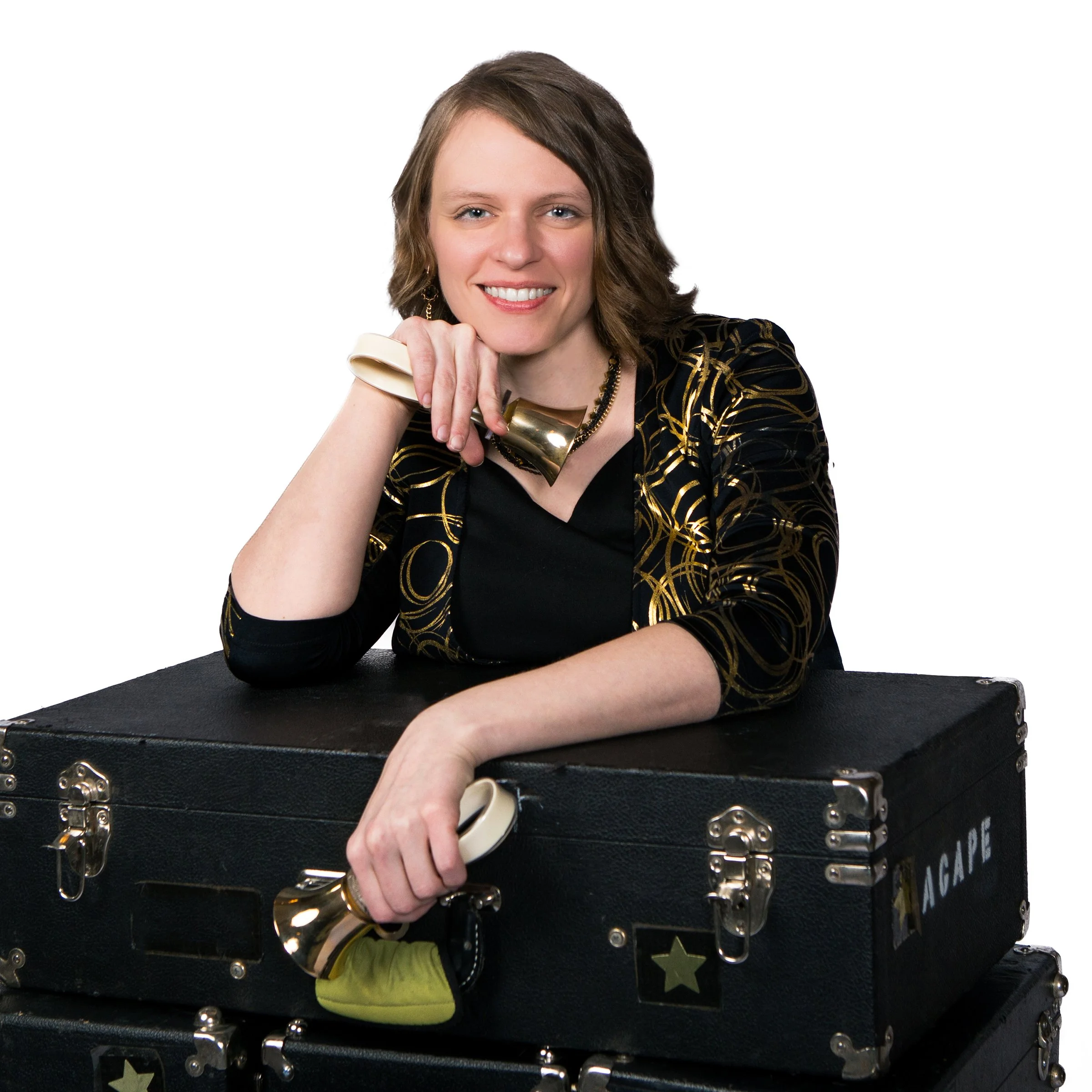 A woman with short brown hair and a black and gold patterned top smiling, sitting behind a black box with metallic accents and star decoration.