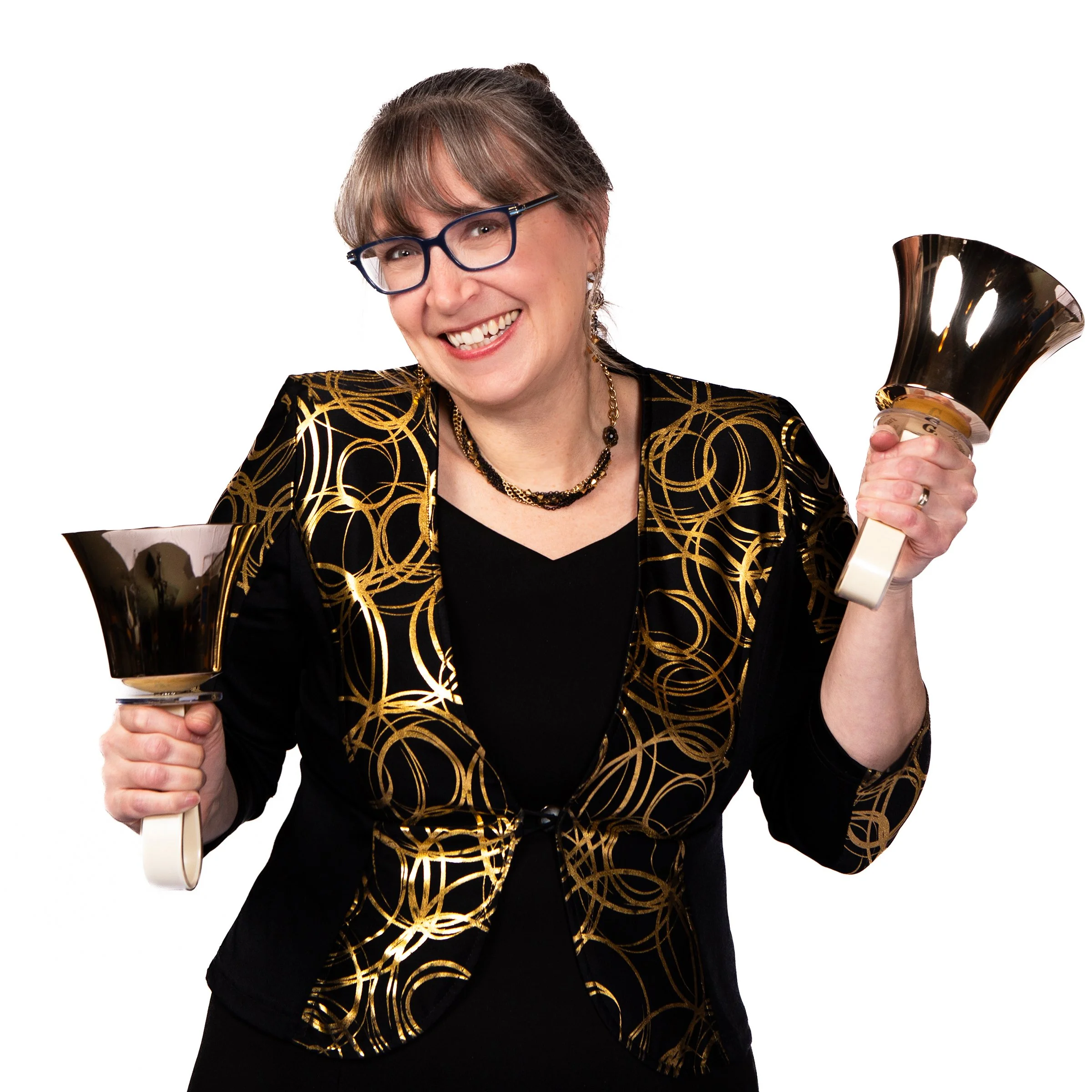 Woman smiling, holding a handbell, wearing glasses and a black and gold patterned outfit.