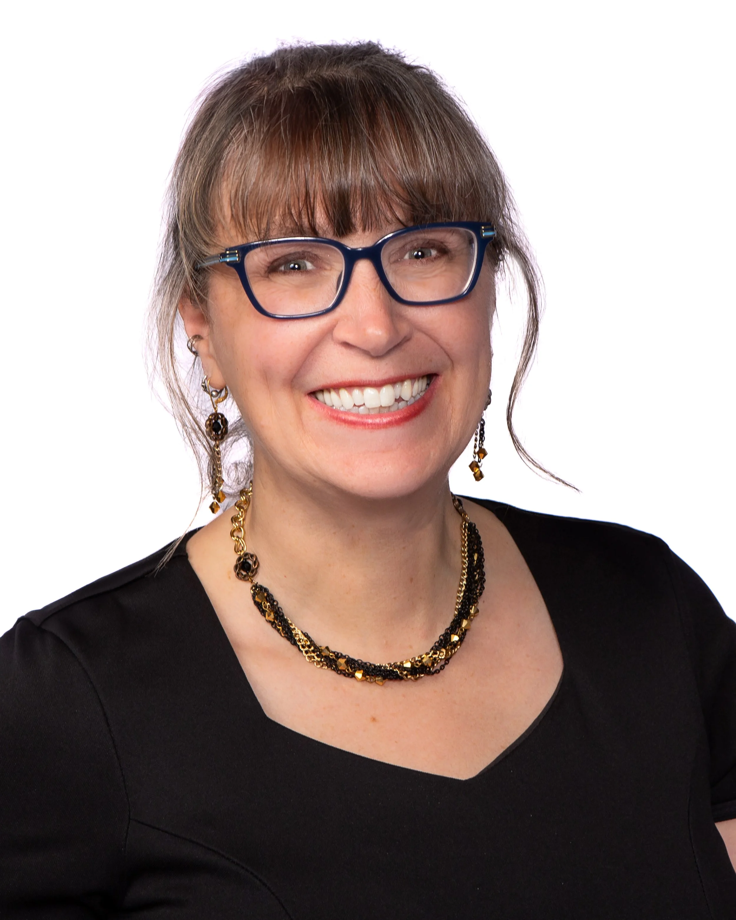 Close-up of a woman with short brown hair, wearing glasses, earrings, and a necklace, smiling against a plain white background.