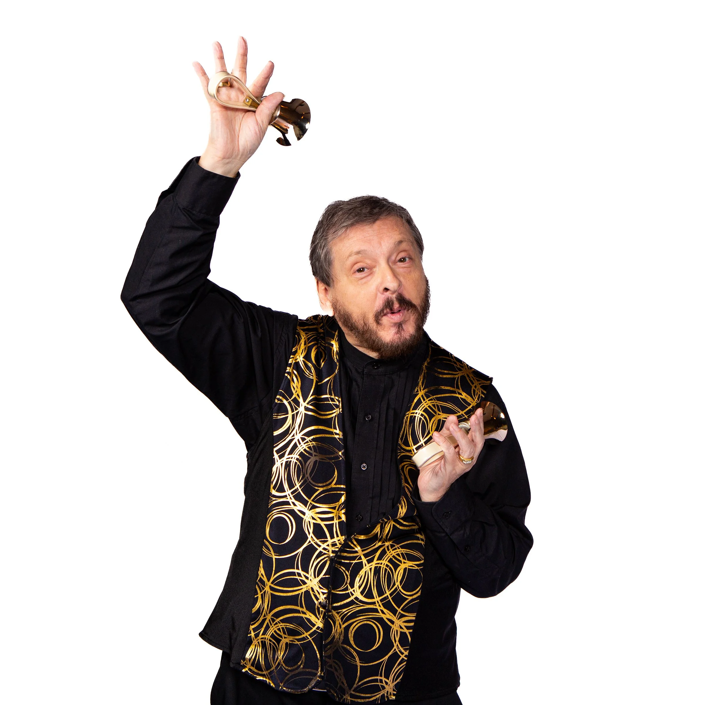 A man with a beard and mustache wearing a black outfit with gold patterns, holding a handbells against a plain white background.