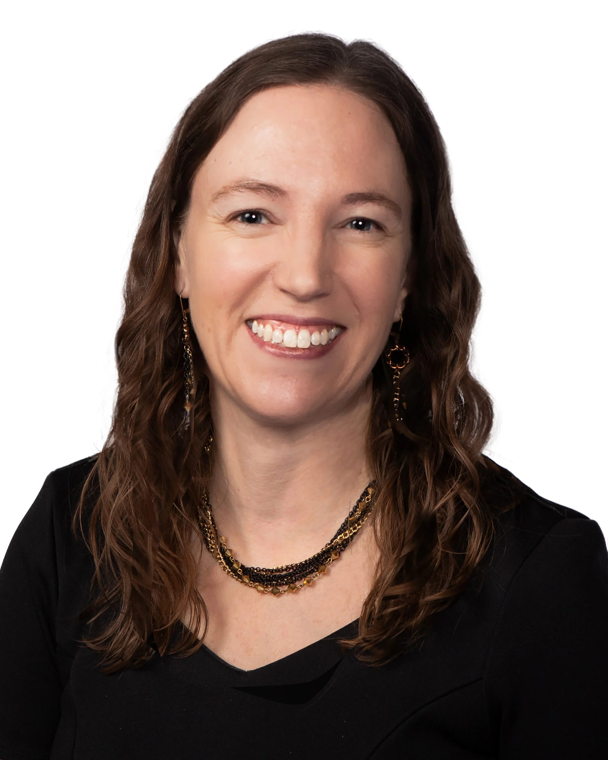 Close-up of a smiling woman with brown hair, wearing black top, gold jewelry, and a white background.