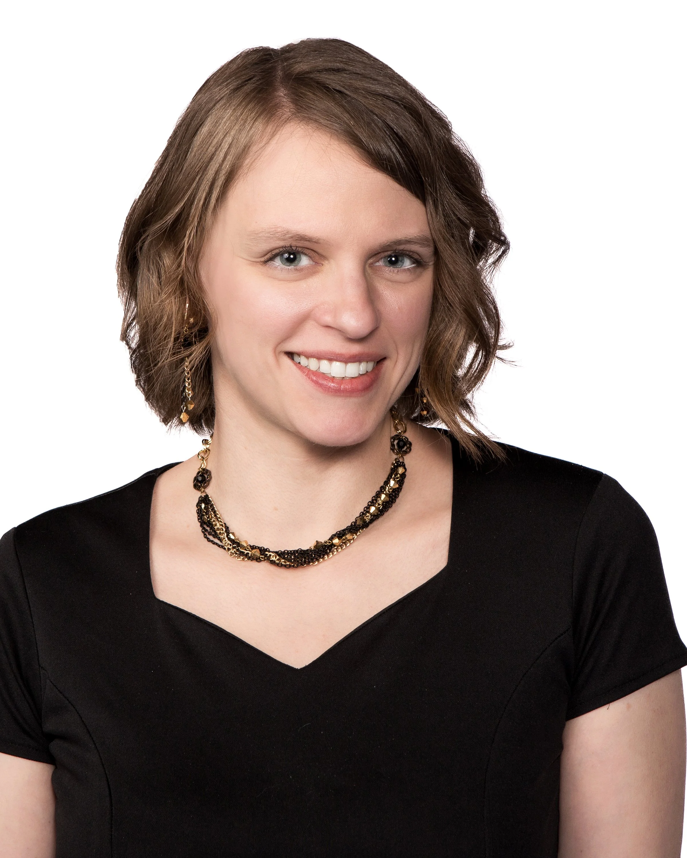 Close-up of a woman with blue eyes and shoulder-length brown hair, wearing a black top and a gold and black necklace, smiling against a white background.