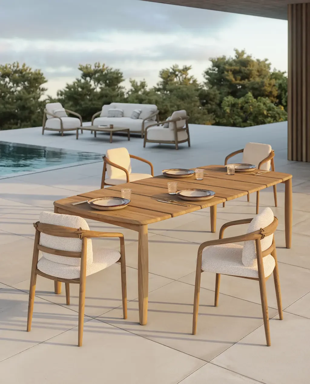 Outdoor patio with a set dining table, four cushioned chairs, pool, lounge seating, and wooded landscape beyond, creating a serene atmosphere.