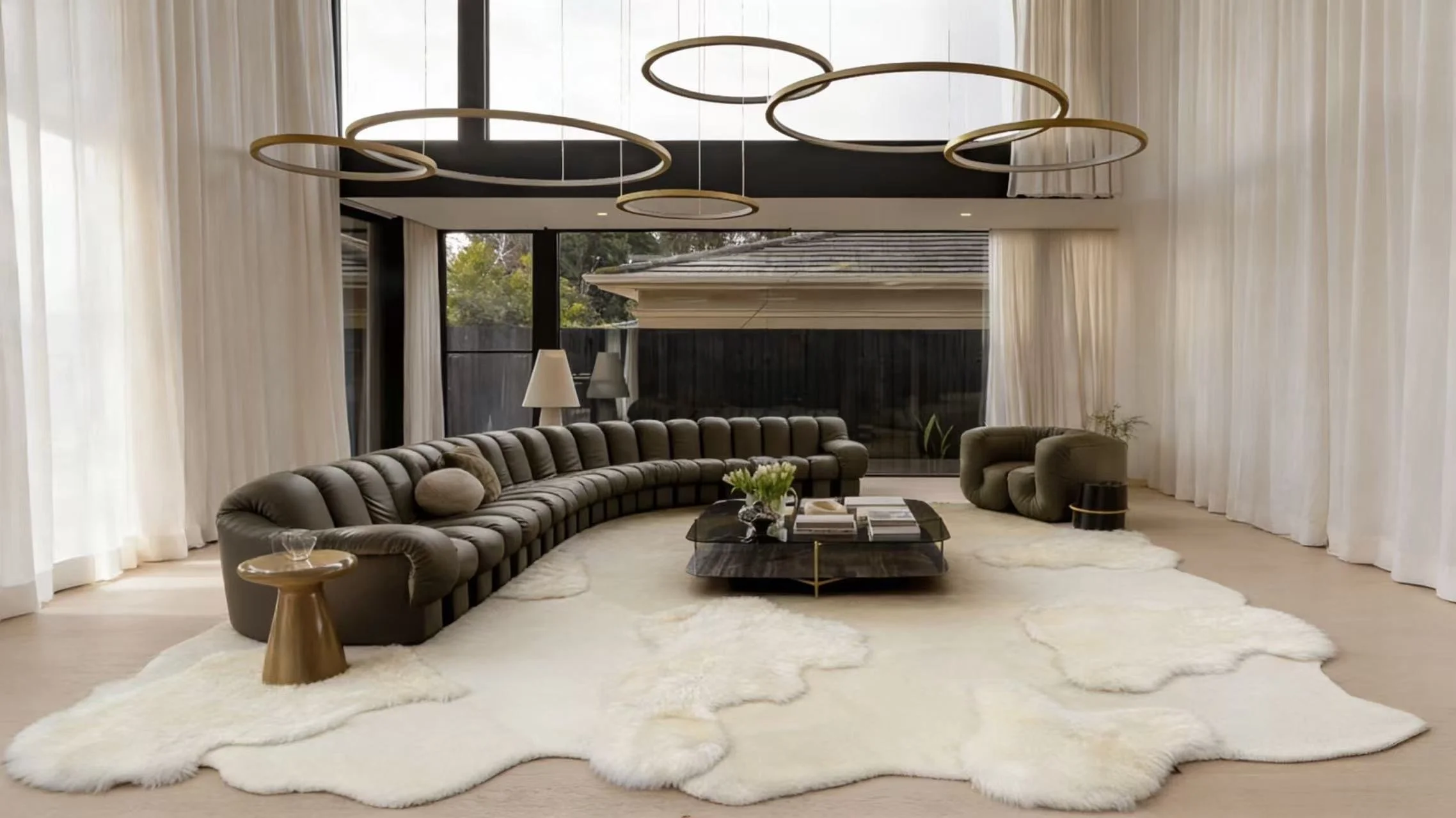 Luxurious modern living room with a curved gray sectional, white fusion rug, sculptural pendant lights, sheer curtains, and calm neutral tones.
