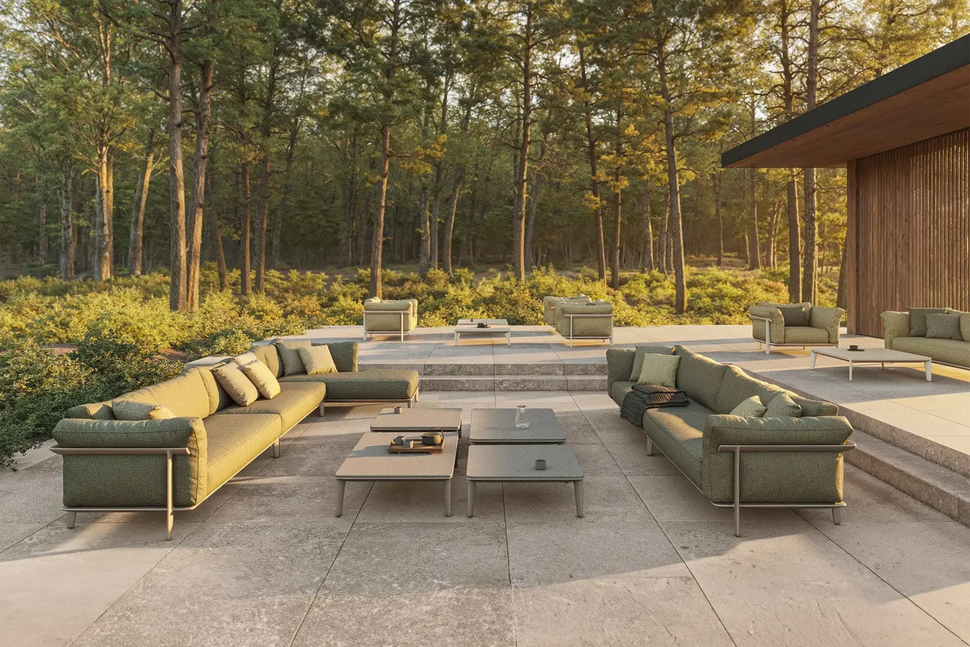 Modern outdoor patio with yellow and green sofas, coffee tables, and steps beside a wood-clad home, surrounded by a serene sunlit forest.