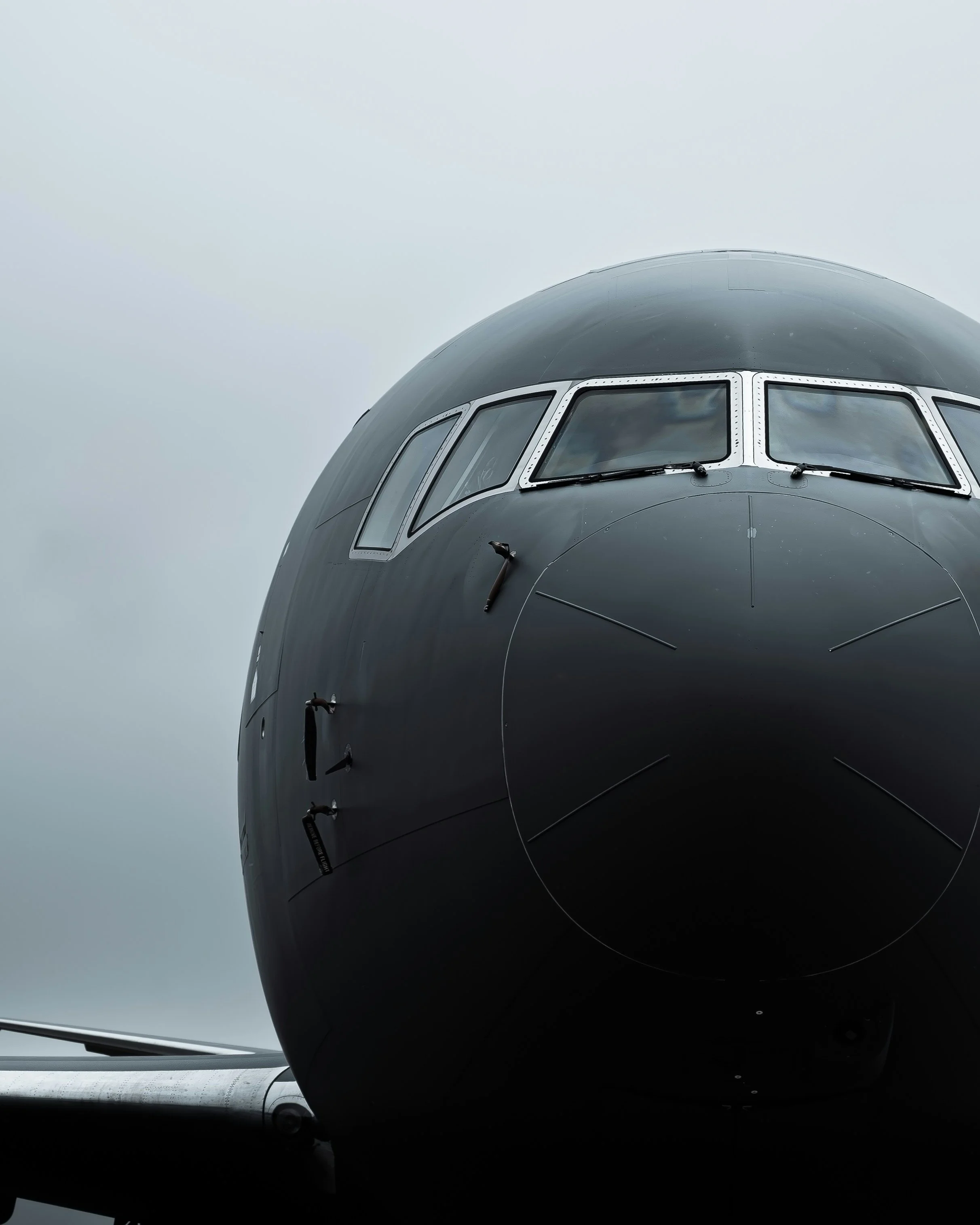 Close-up of an airplane nose, showing cockpit windows and part of the fuselage, with a cloudy sky background.
