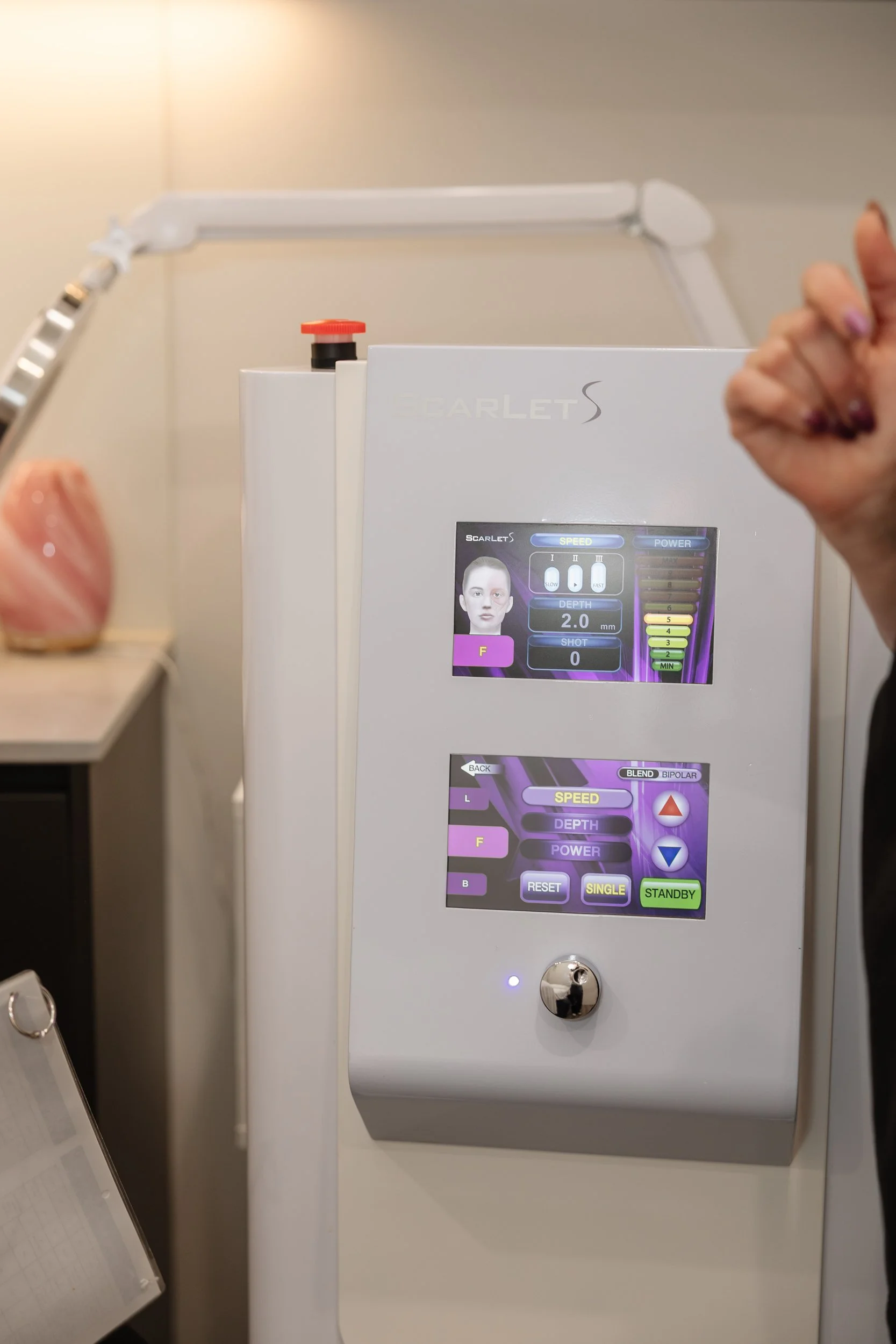 Medical device with a touchscreen display showing settings for speed, depth, and other parameters, with a person giving a thumbs up and a hand in the foreground.