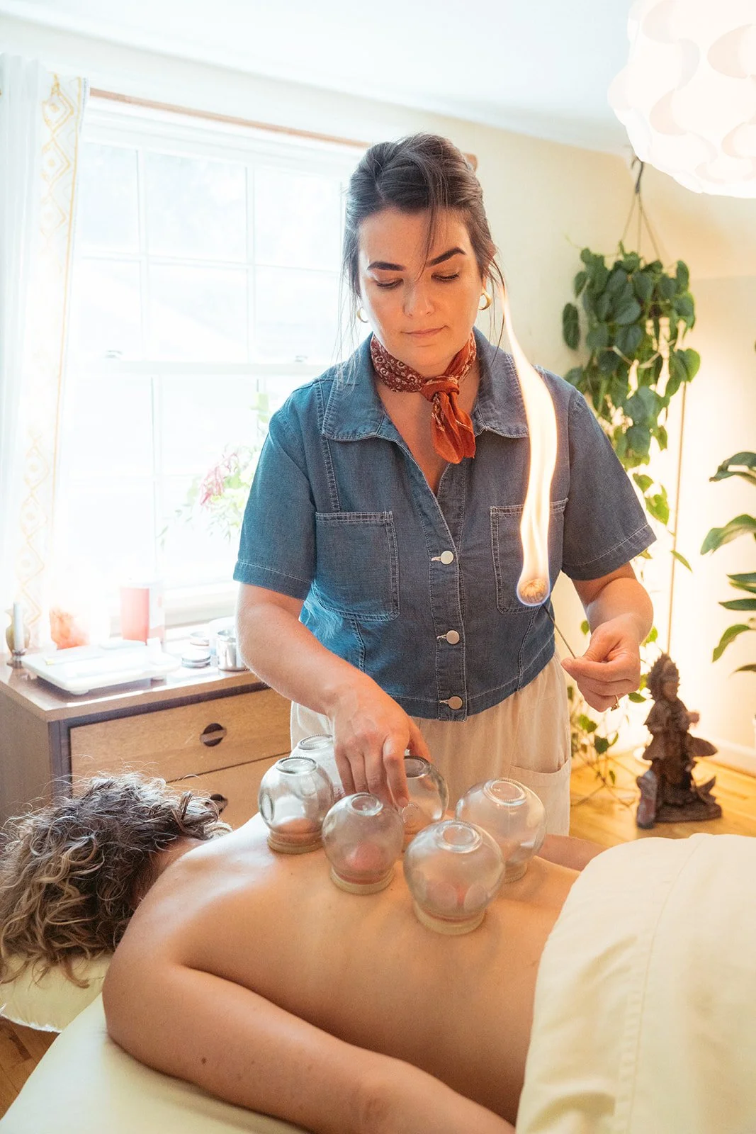Woman receiving an cupping therapy treatment from a practitioner in a well-lit room with plants and natural light.