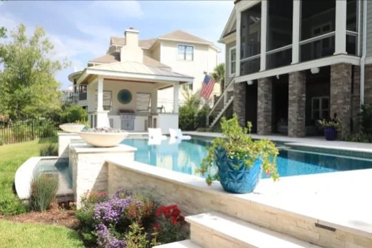 Residential backyard with a swimming pool, landscaped garden, and houses in the background.