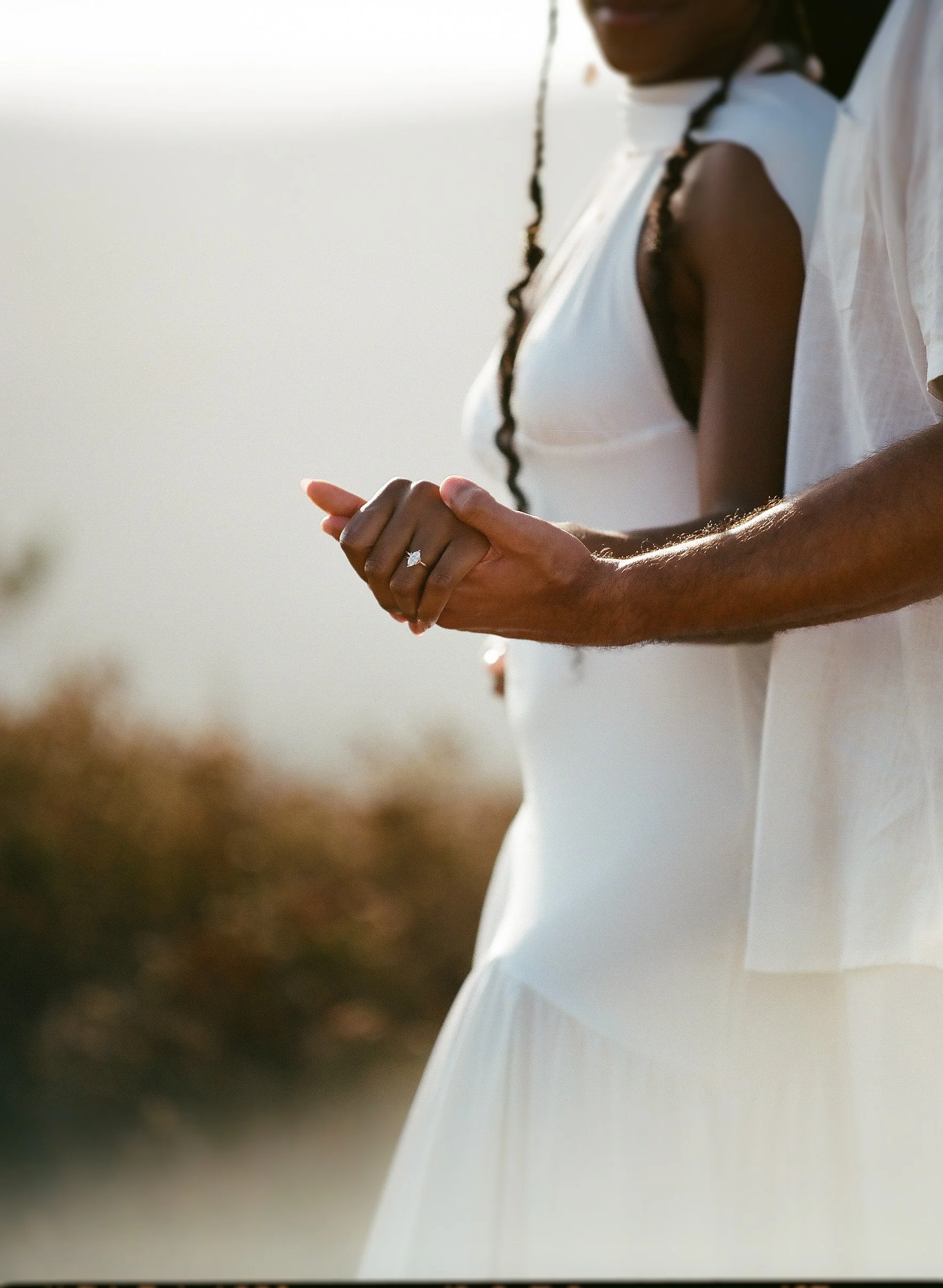 Close-up of a woman wearing a white dress and a ring on her finger, holding her hands together.