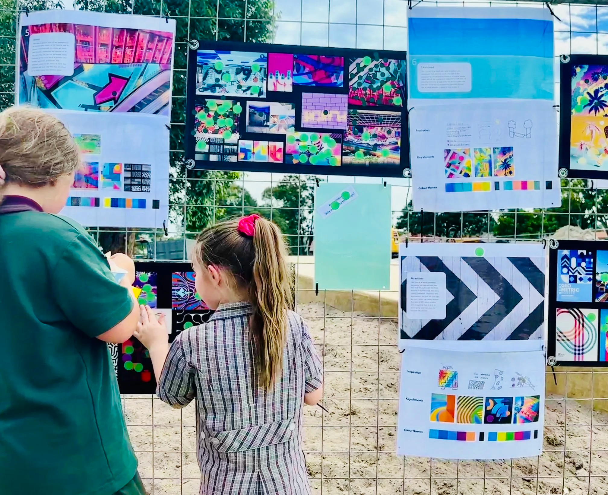 People viewing colorful art and design posters displayed on a metal grid at an outdoor exhibition.