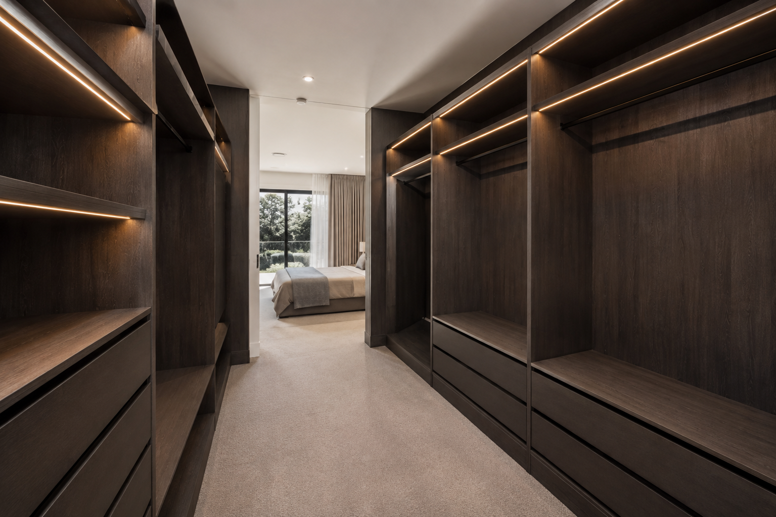 View of a modern walk-in closet with dark wooden shelves and drawers, leading to a bedroom with a bed, large window, and beige curtains.