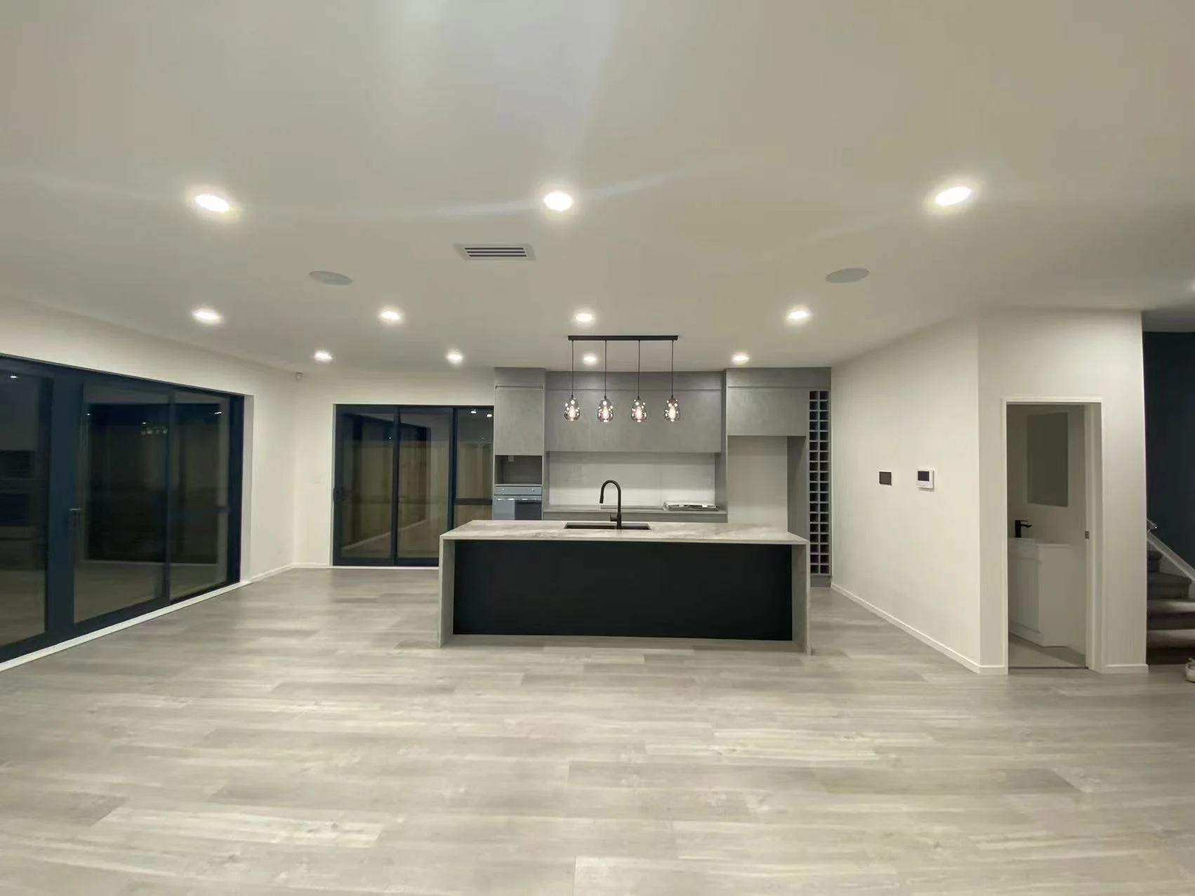 Empty modern kitchen with an island, grey cabinetry, and large sliding glass doors leading outside.
