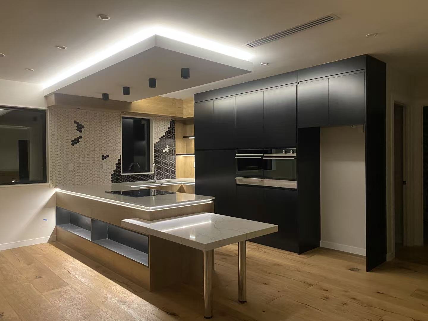 Modern kitchen with black cabinets, marble countertop island, mosaic tile backsplash, and wooden flooring.