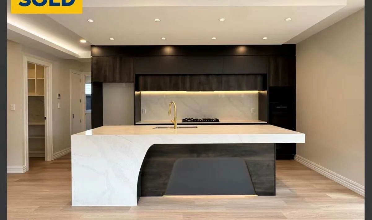 Modern kitchen with dark wood cabinets, a white marble island with a gold faucet, and a built-in stove. The space features recessed lighting and a light wood floor.