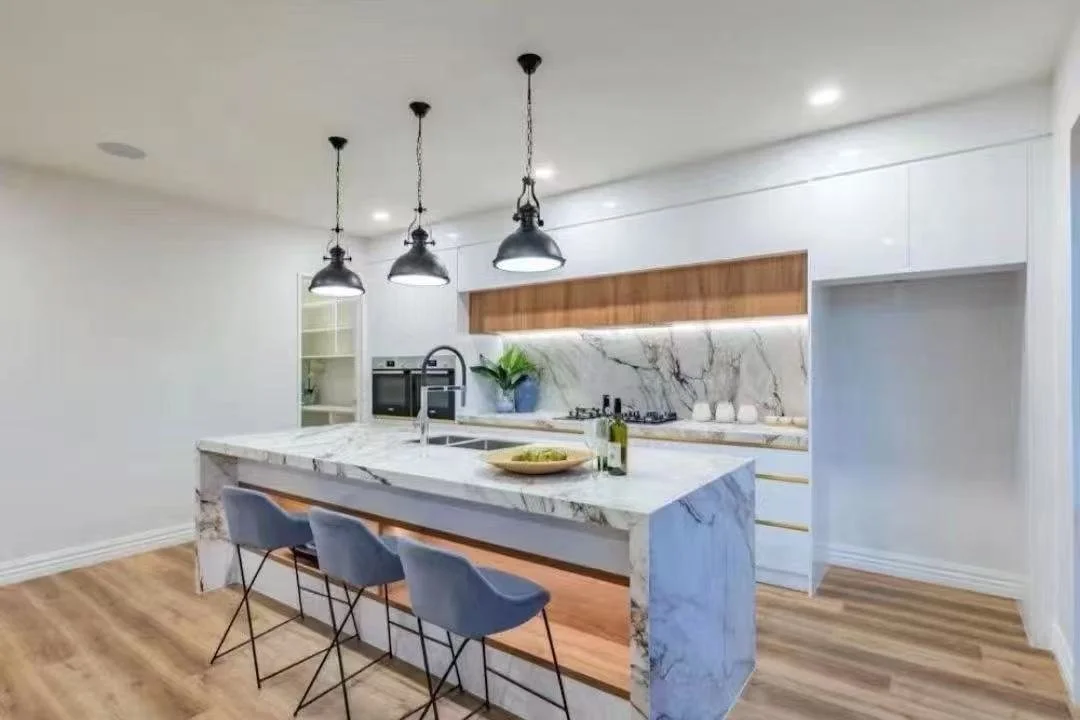 Modern kitchen with white cabinets, marble island, wooden accents, black pendant lights, and hardwood floors.