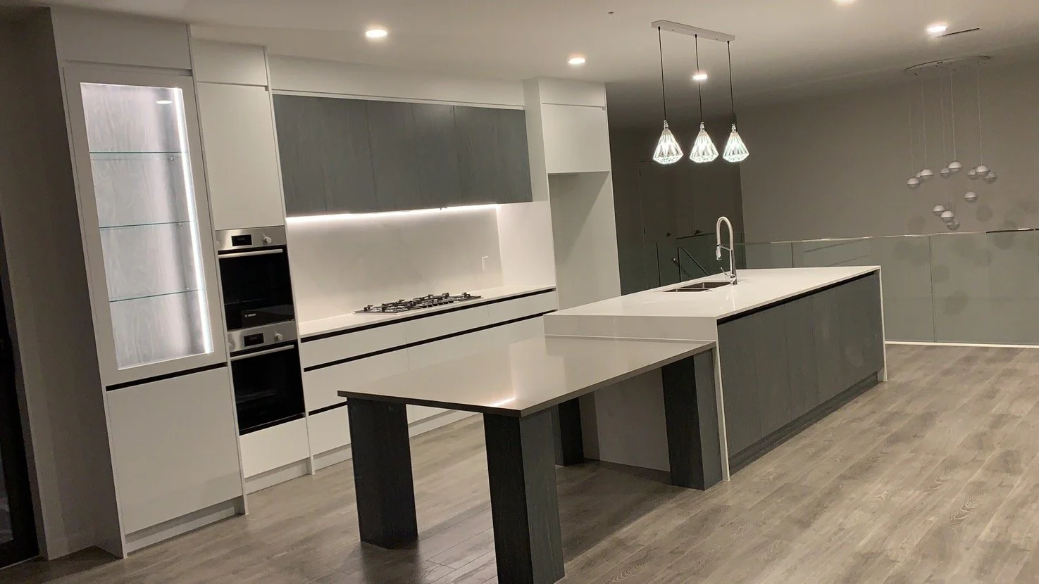 Modern kitchen with white and gray cabinetry, a kitchen island with a sink, pendant lights above, and wood flooring.