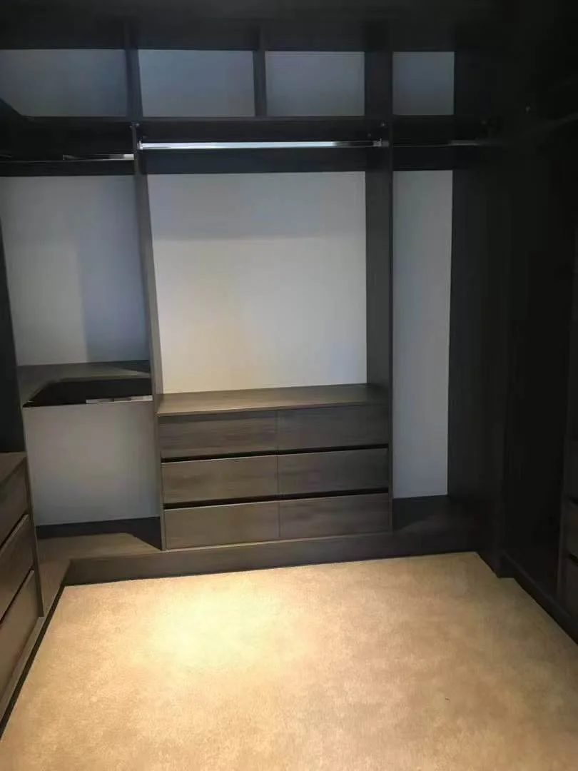 Empty walk-in closet with dark wood shelves, drawers, and hanging space, beige carpeted floor.