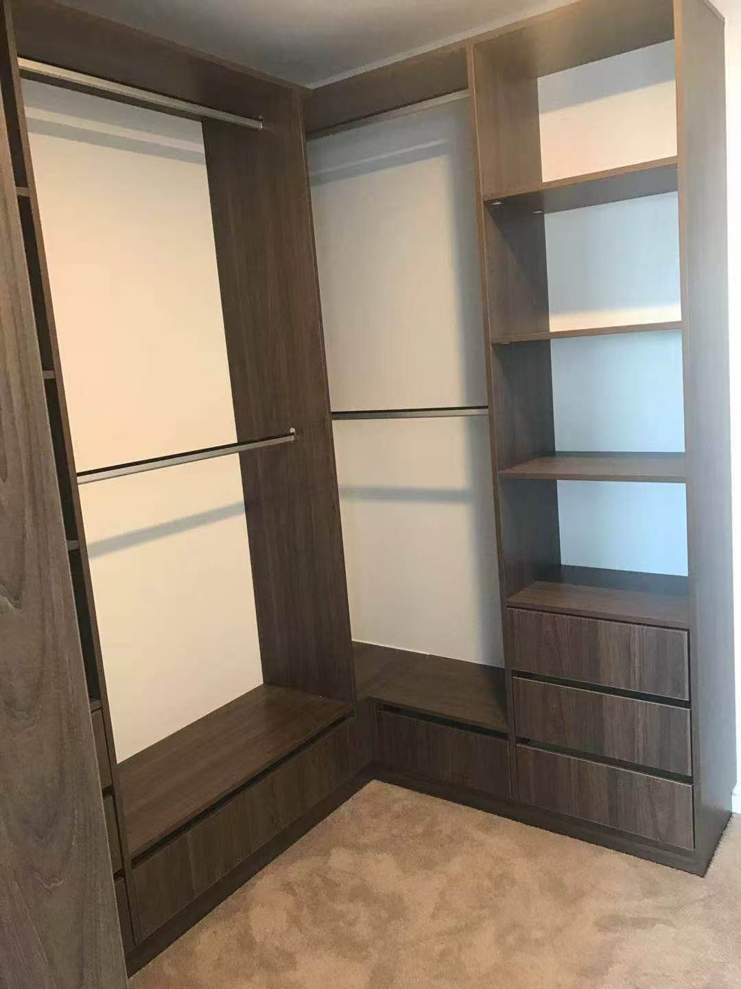 Empty walk-in closet with dark wood shelving, hanging rods, and drawers, beige carpeted floor.