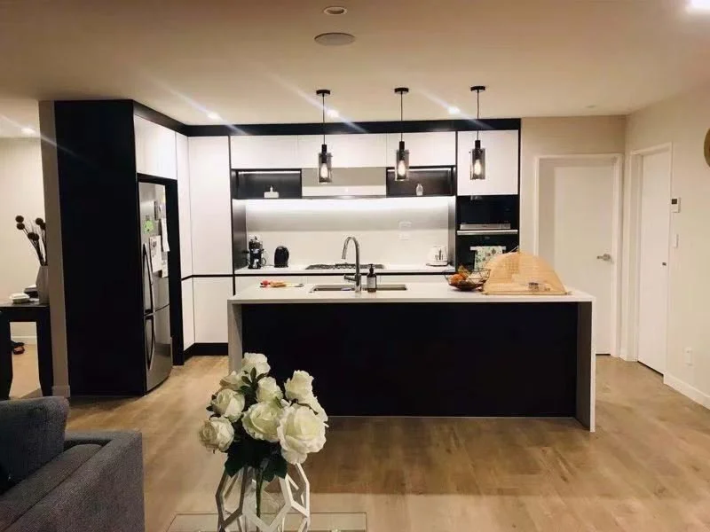 Modern kitchen with black and white cabinetry, island with sink, pendant lights, stainless steel refrigerator, and a bouquet of white roses in the foreground.