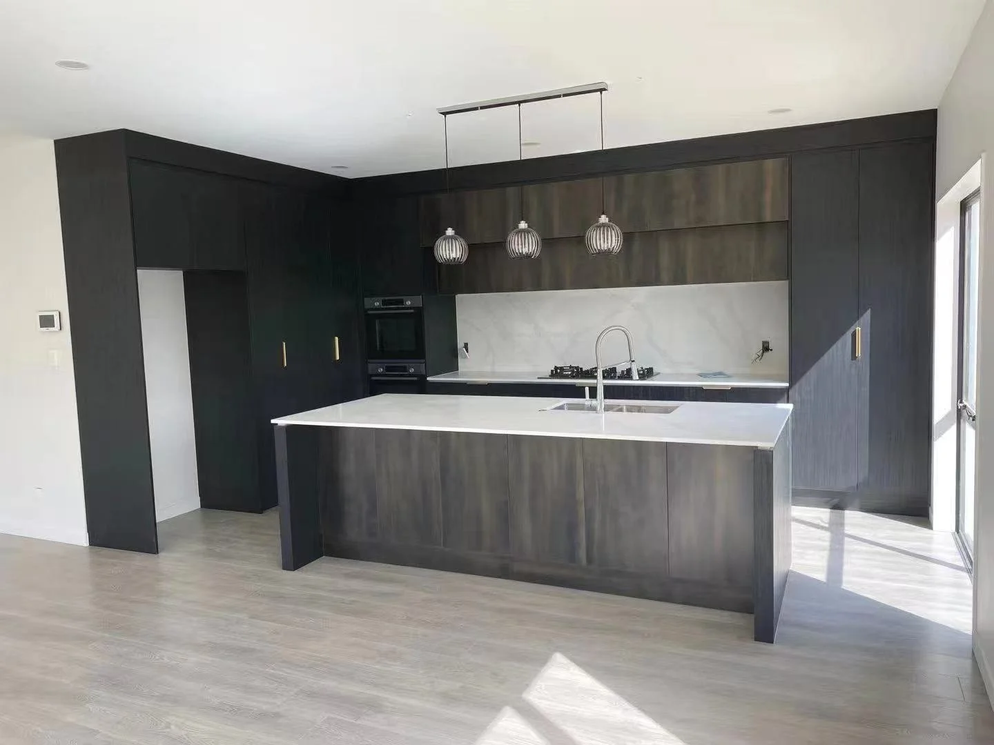 Modern kitchen with dark wood cabinets, white countertop, built-in oven, and pendant lights over island with sink.